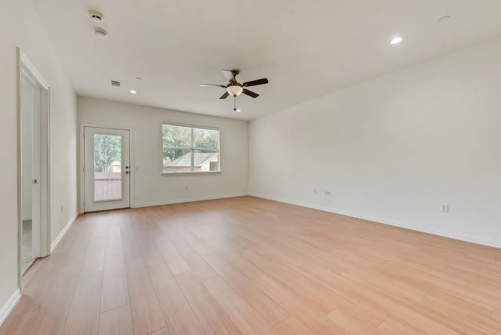 Spacious open-concept living area featuring wood-finish flooring, a ceiling fan with integrated lighting, and recessed lighting