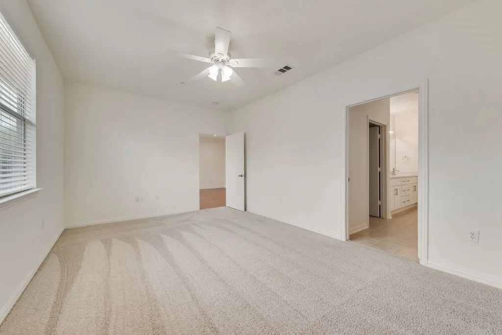 Spacious room featuring neutral carpet flooring, a ceiling fan, and a window with blinds