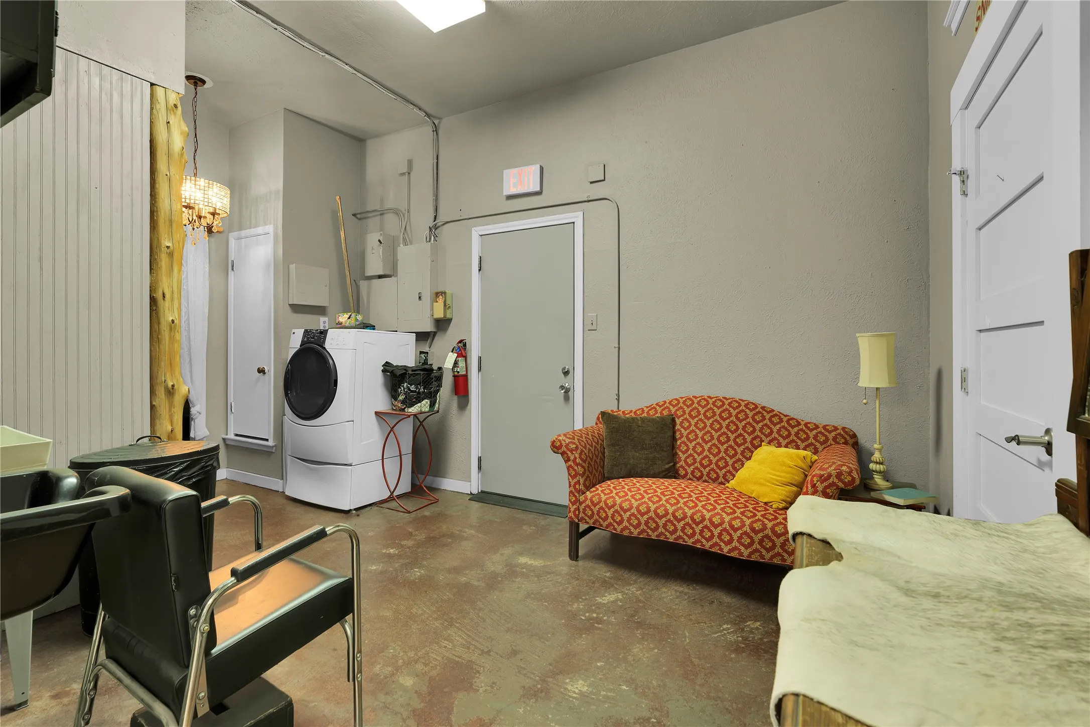 Utility area featuring durable concrete flooring, a front-loading washer, and a ceiling-mounted fluorescent light fixture
