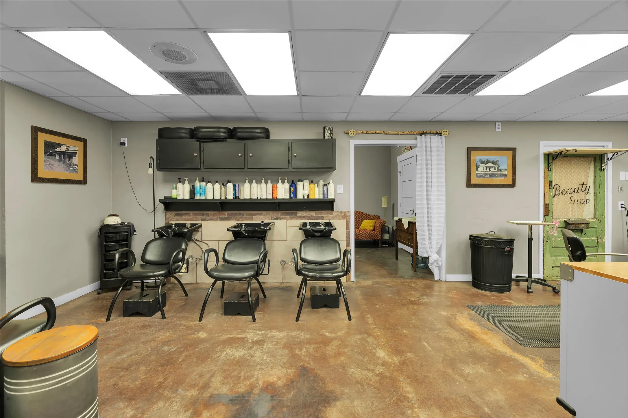 Commercial space featuring drop ceiling with recessed lighting, exposed concrete flooring, light gray walls, and an accent wall with brick-finish paneling