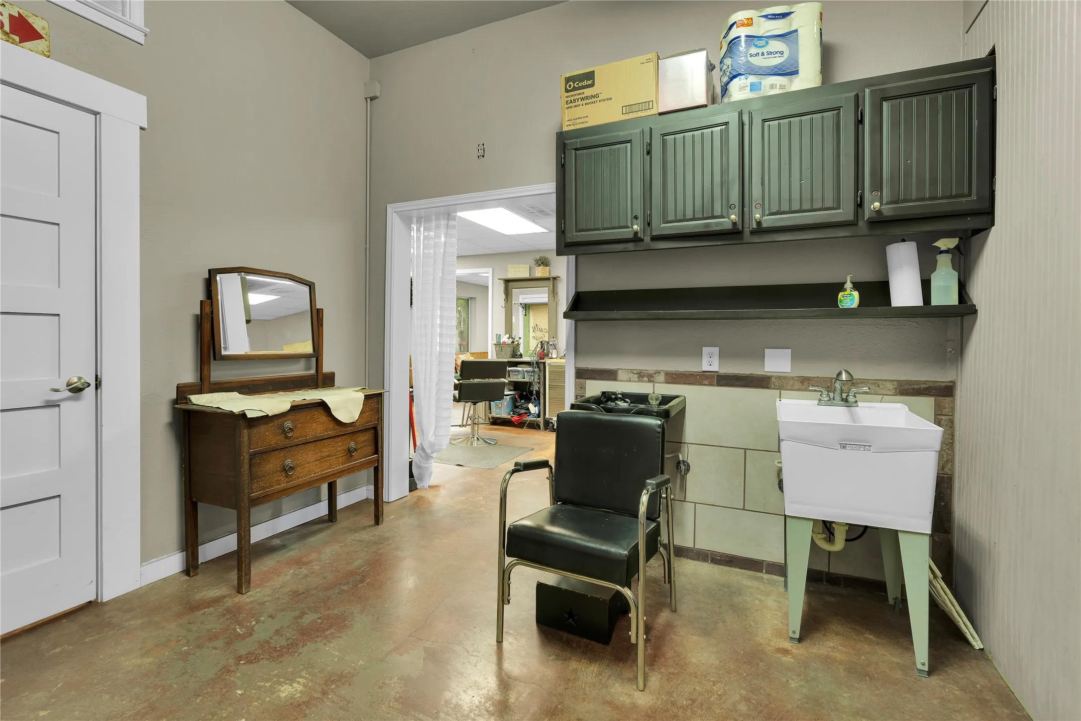 Spacious room featuring concrete flooring, a utility sink, and wall-mounted cabinetry for storage