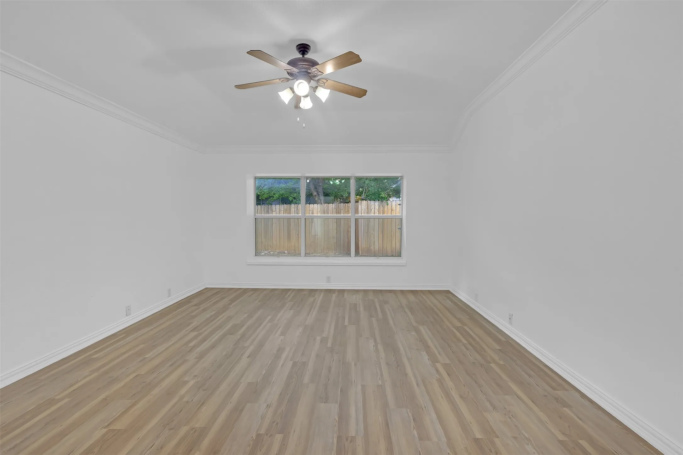 Empty room featuring light wood-style flooring, crown molding, and a ceiling fan