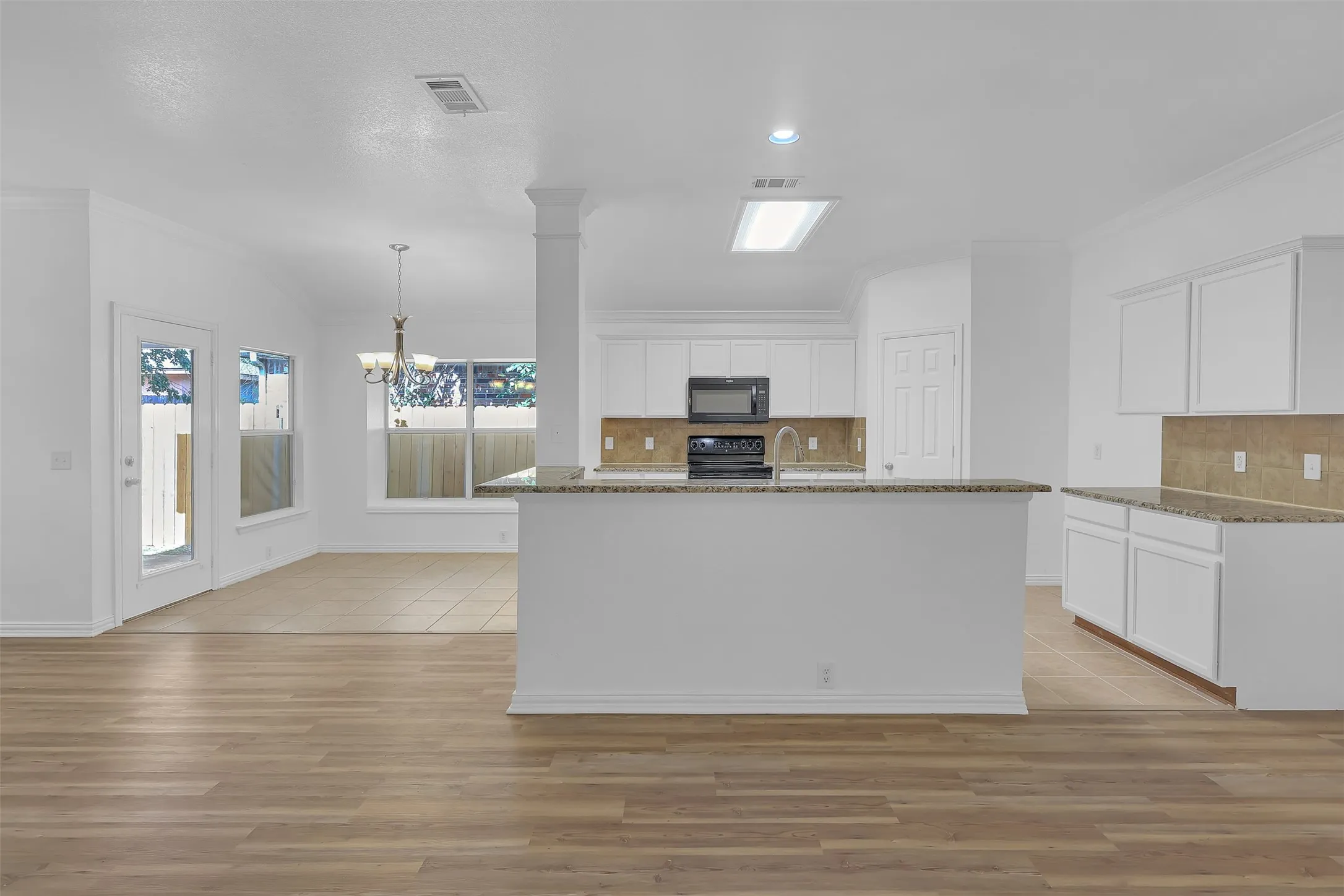 Kitchen with black appliances, white cabinetry, crown molding, stone countertops, and light wood-type flooring
