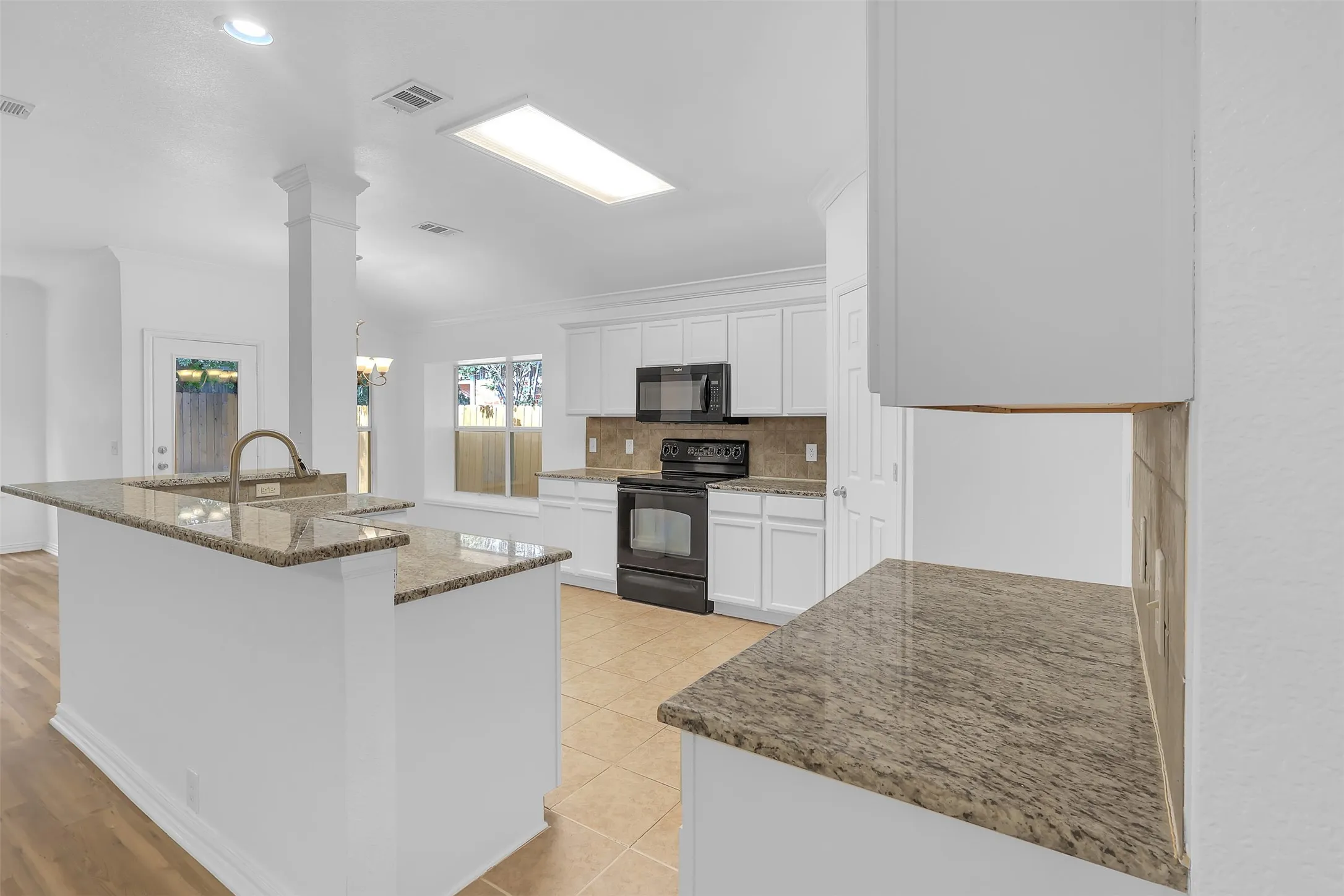 Kitchen featuring black appliances, stone countertops, backsplash, ornamental molding, and white cabinetry