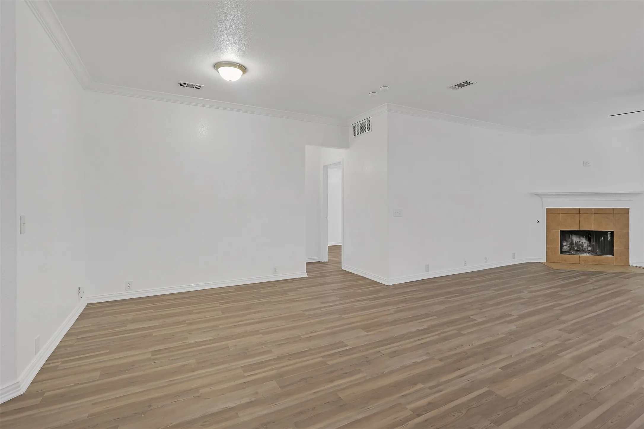 Unfurnished living room featuring light wood-type flooring, ornamental molding, and a tile fireplace