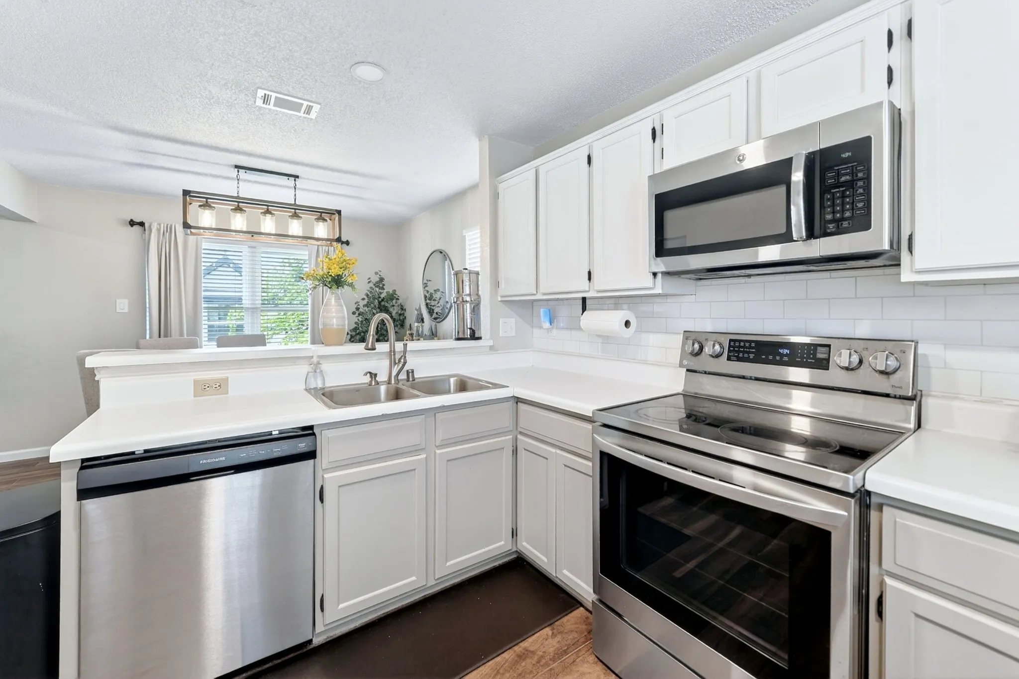 Kitchen featuring stainless steel appliances, white subway tile backsplash, white countertops, and white cabinetry
