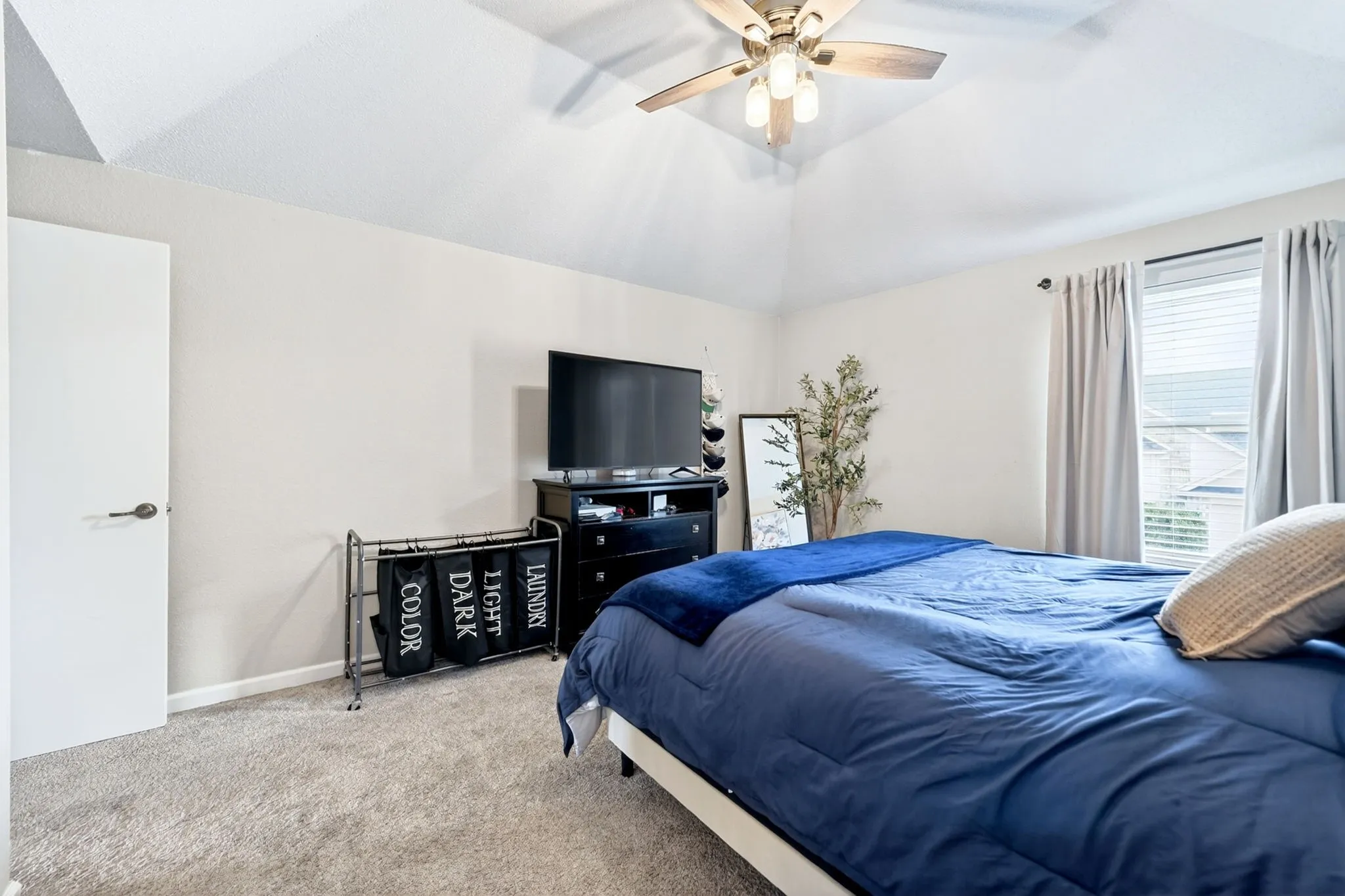 Vaulted ceiling bedroom featuring a ceiling fan with light fixture, neutral wall paint, and carpet flooring