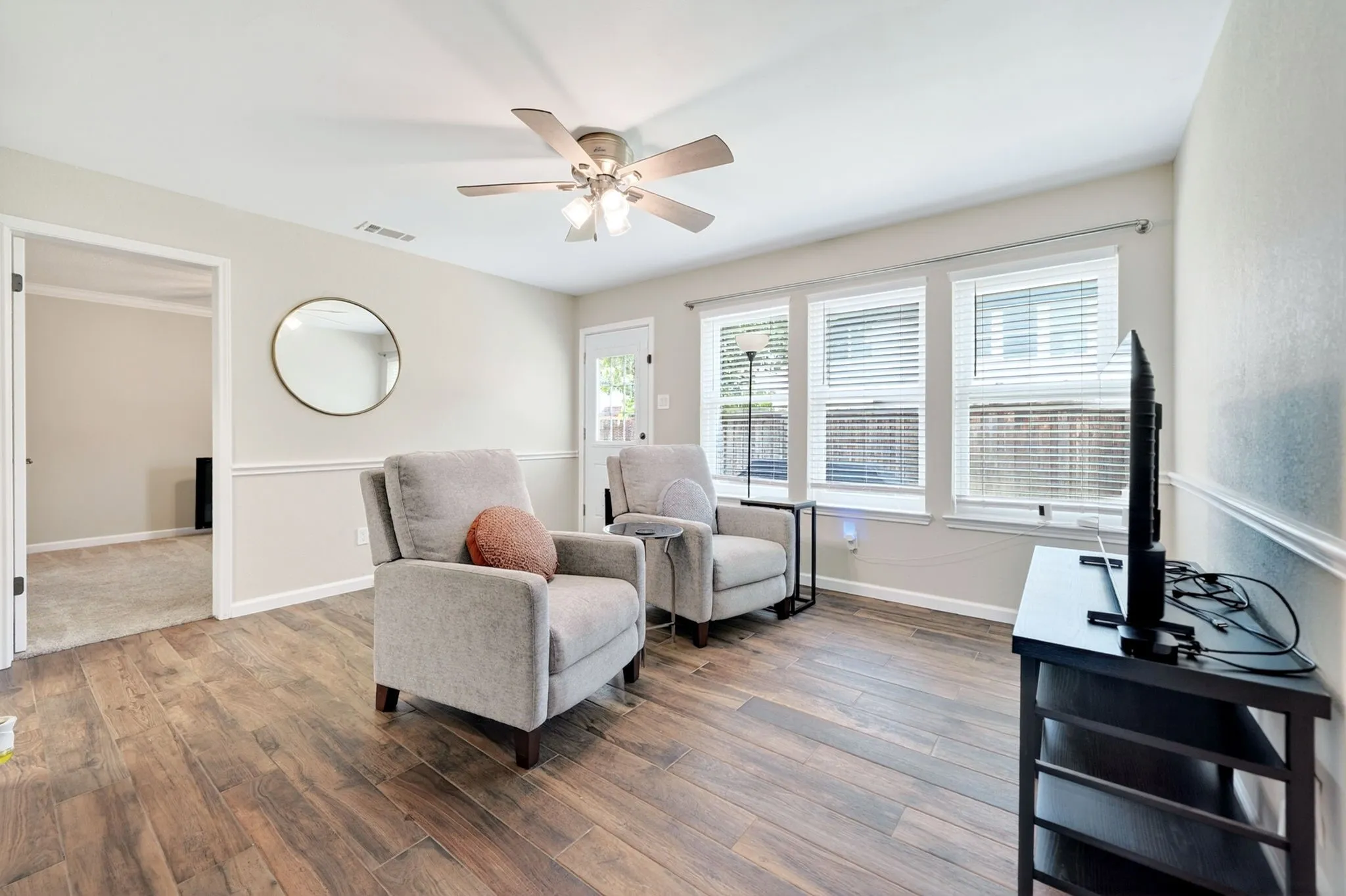 Spacious living area featuring wood-finish flooring, a ceiling fan, and three large windows with blinds