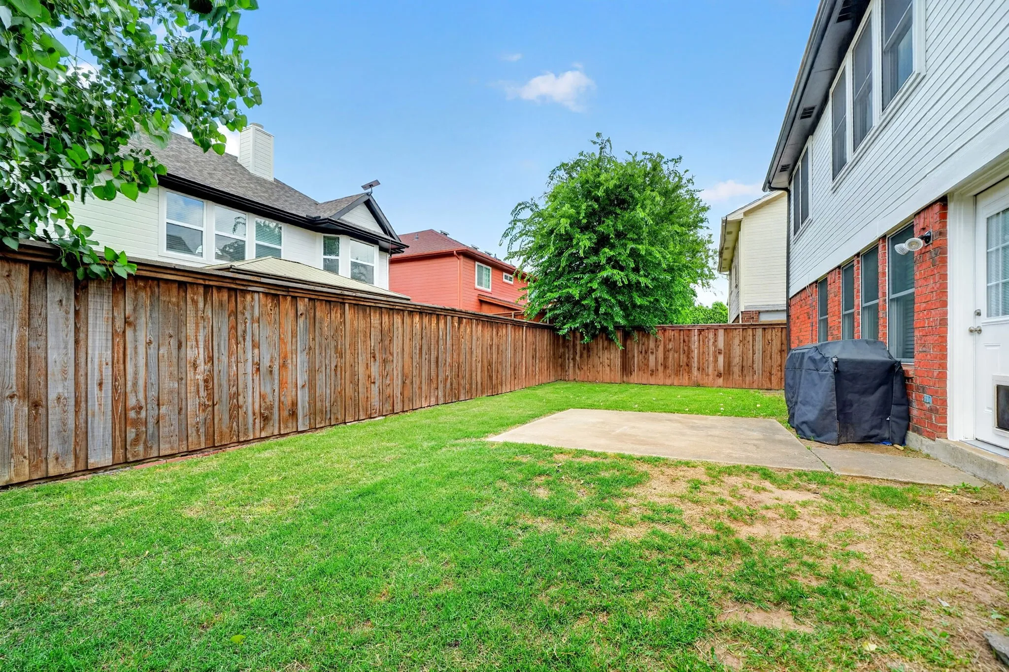 Private backyard featuring a wood privacy fence, concrete patio, and a grass area