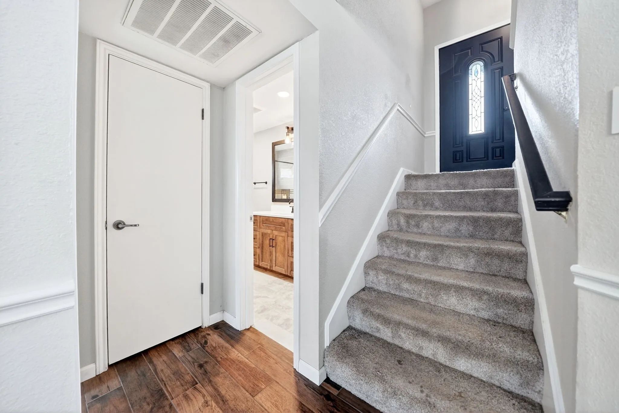 Entryway featuring wood-finish flooring, a carpeted staircase with a dark wood handrail, and a decorative paneled front door with leaded glass