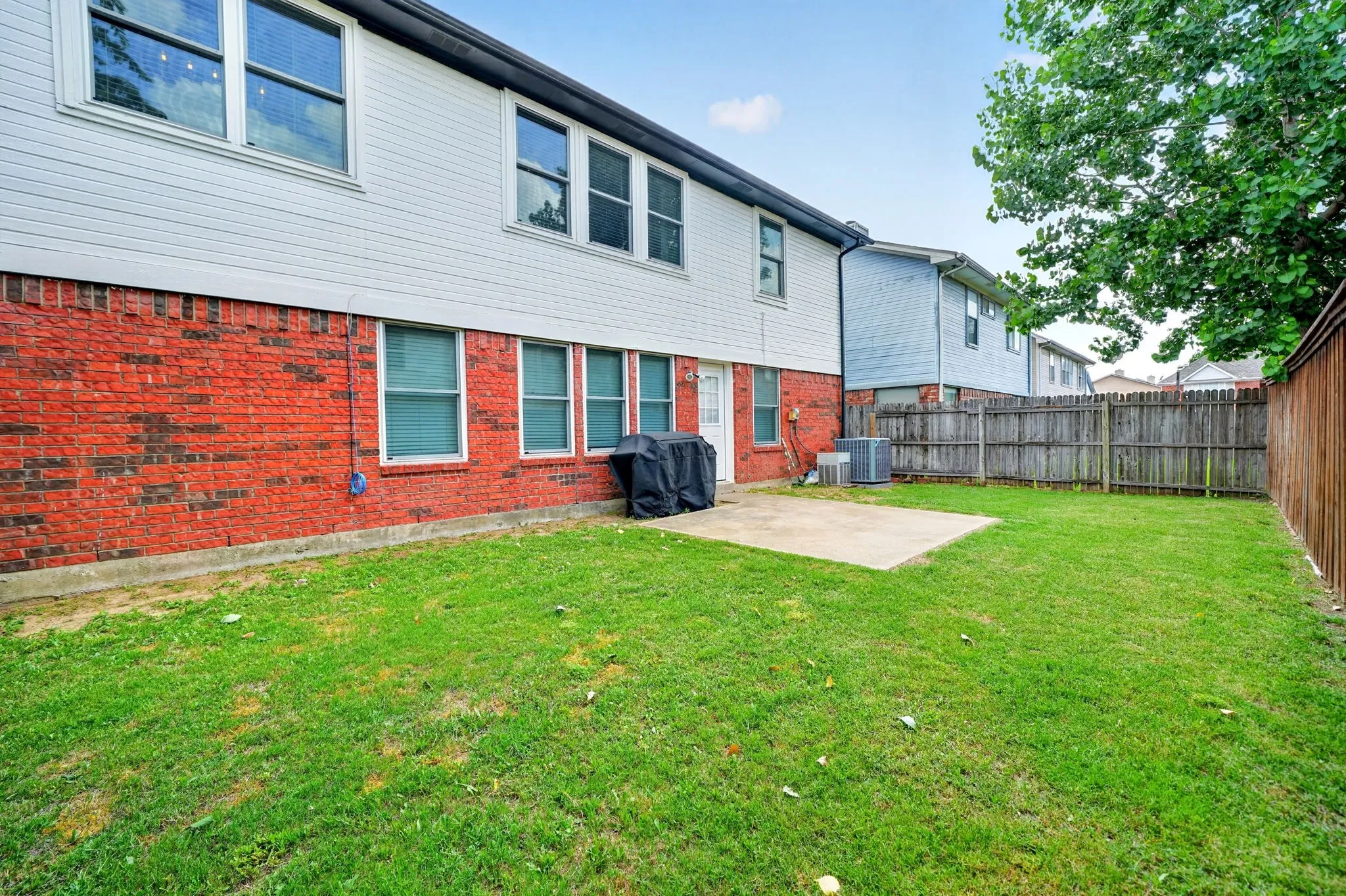 Expansive backyard featuring a rectangular concrete patio, privacy fencing, and a red brick lower exterior with white siding above