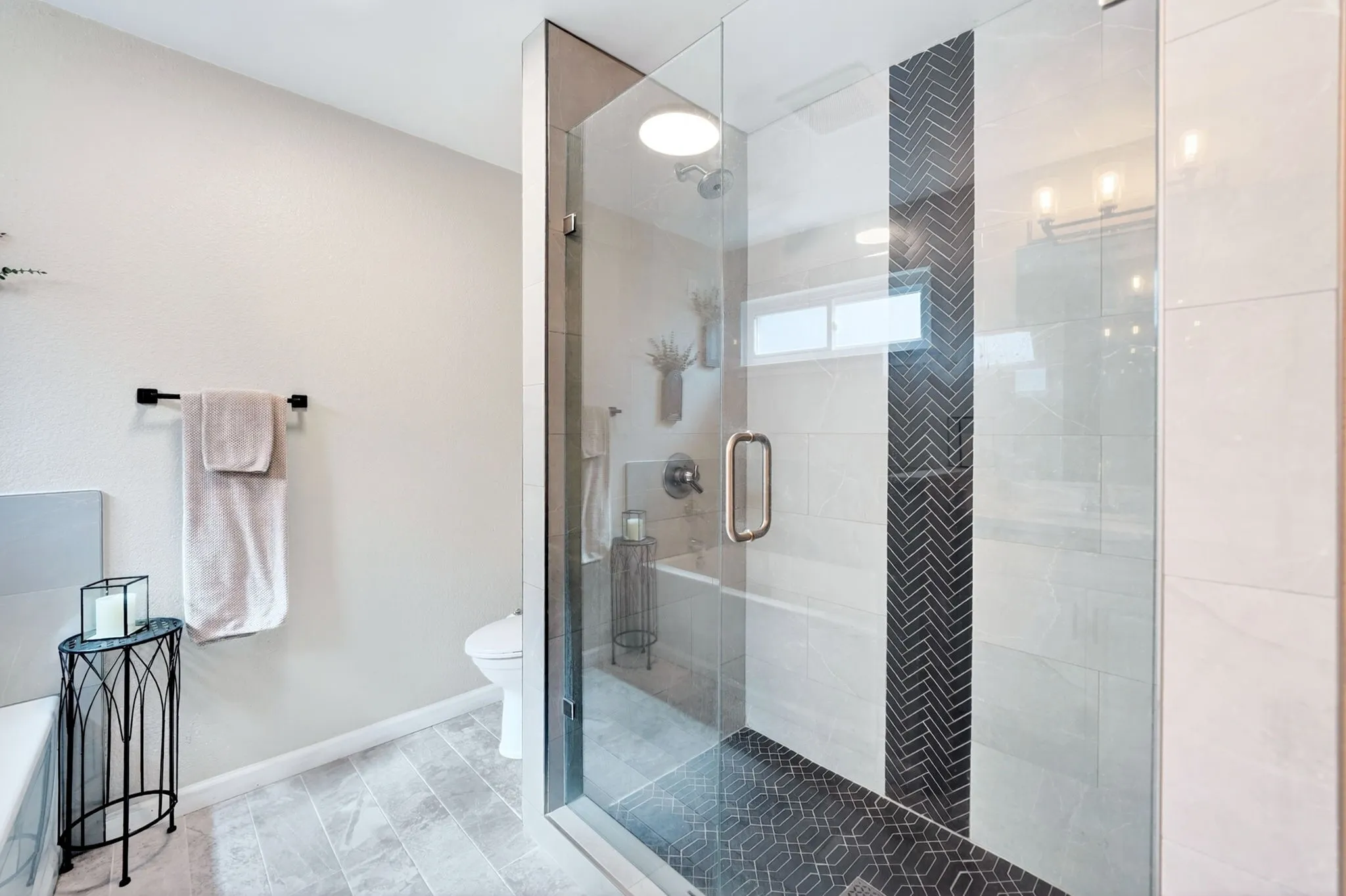 Walk-in shower featuring a glass enclosure, a dark herringbone tile accent wall, and a hexagonal patterned floor