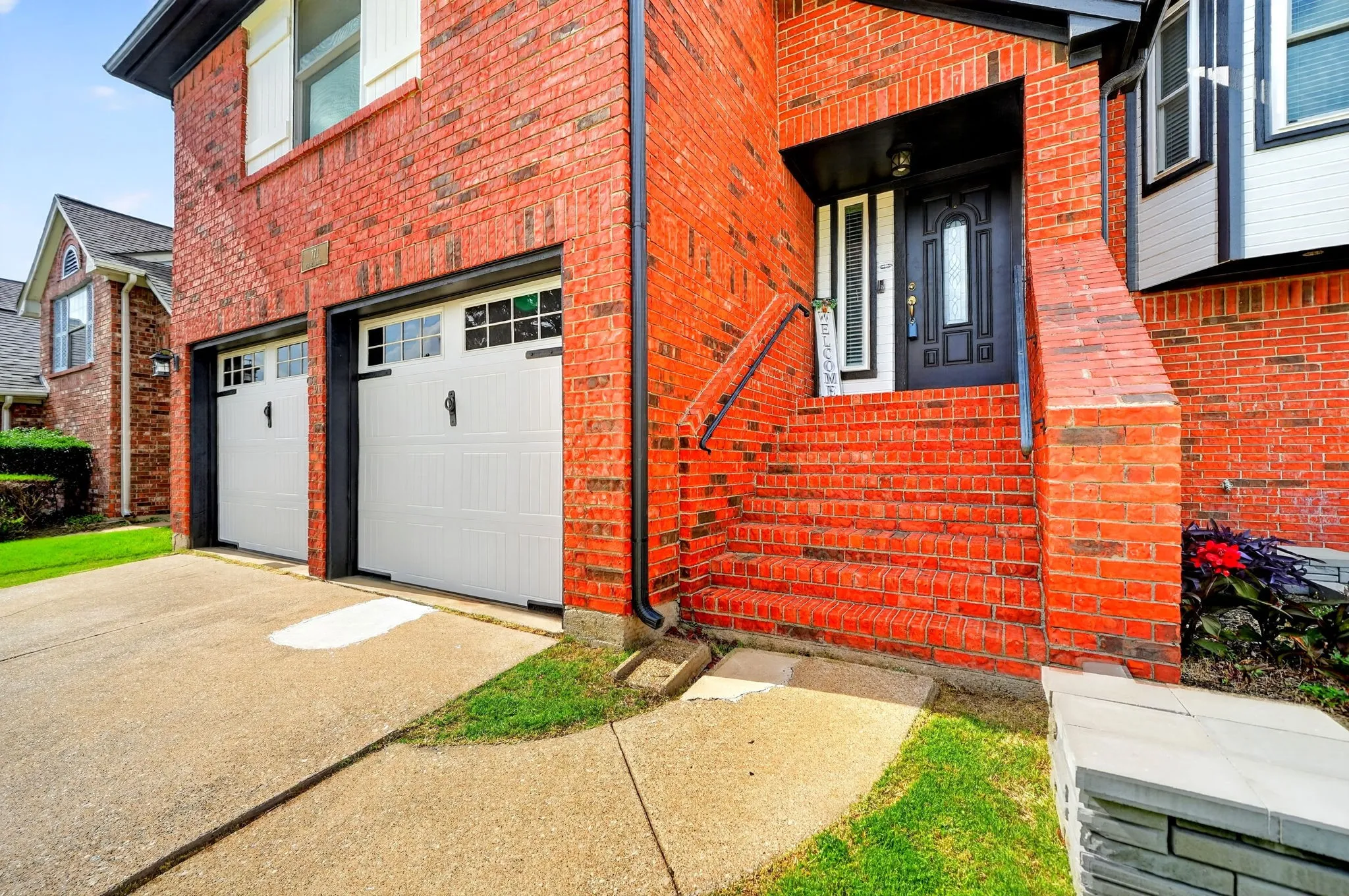 Red brick exterior featuring a multi-pane front door, brick stairs with handrails, and a two-car garage with white doors