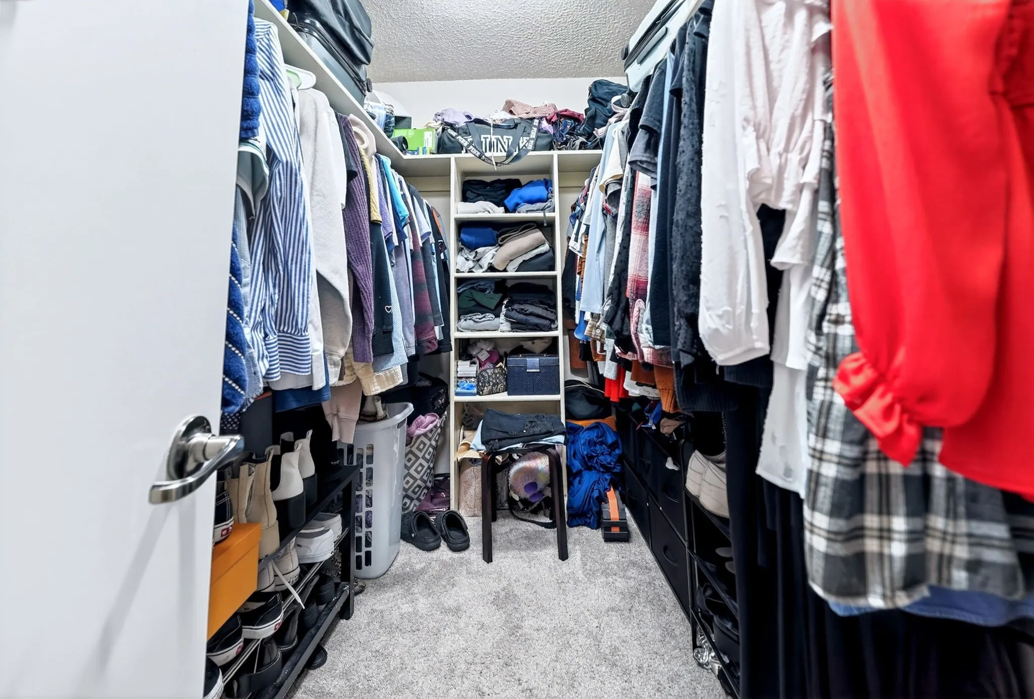 Walk-in closet featuring extensive built-in shelving, multiple hanging rods, and light-toned carpet flooring