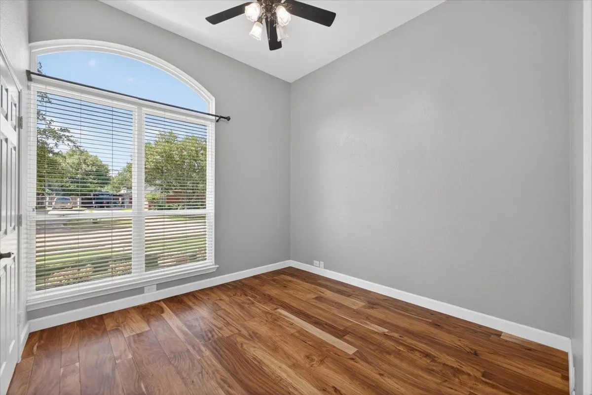 Room featuring an arched window with blinds, wood-finish flooring, light gray walls, white baseboards, and a ceiling fan