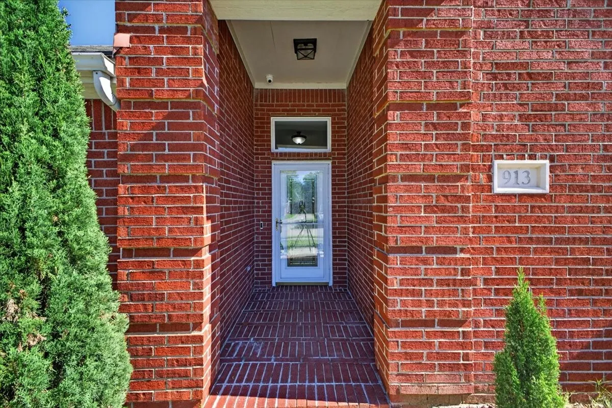 Brick exterior entry featuring a glass panel door with storm door, recessed overhead lighting, and brick flooring