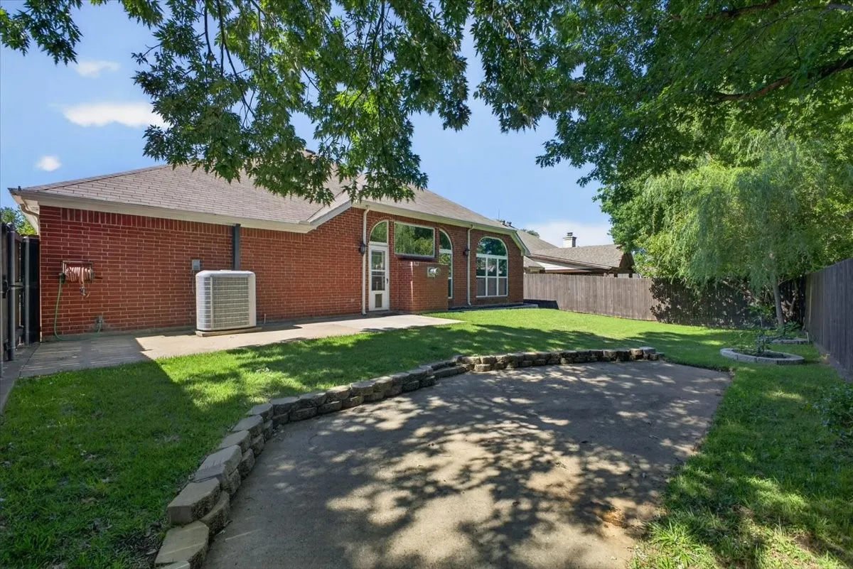 Expansive backyard featuring a manicured lawn, an outdoor patio space with stone retaining wall, and mature trees providing natural shade