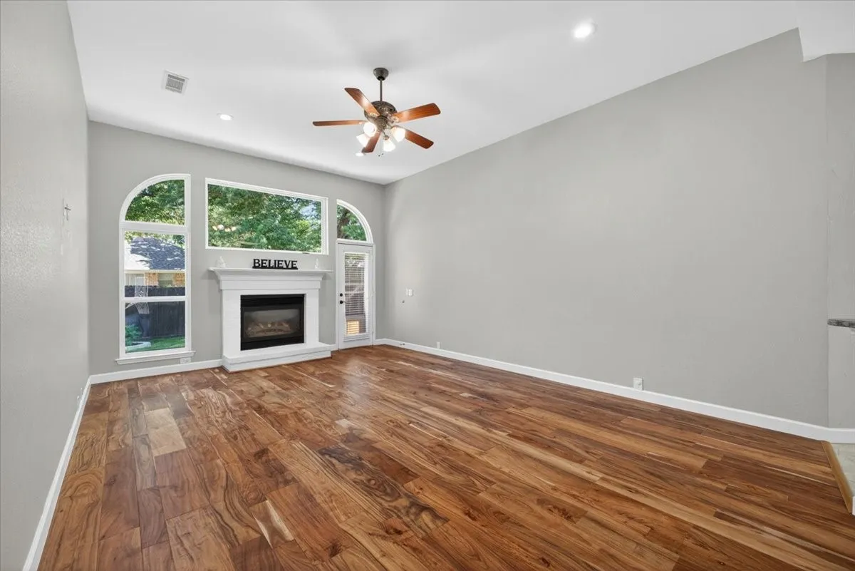 Spacious room featuring wood-finish flooring, a white mantel fireplace, and a vaulted ceiling with a ceiling fan