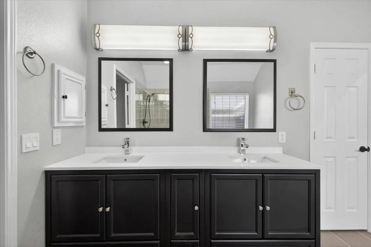 Double vanity featuring black cabinetry, white countertops, two undermount sinks, and individual framed mirrors