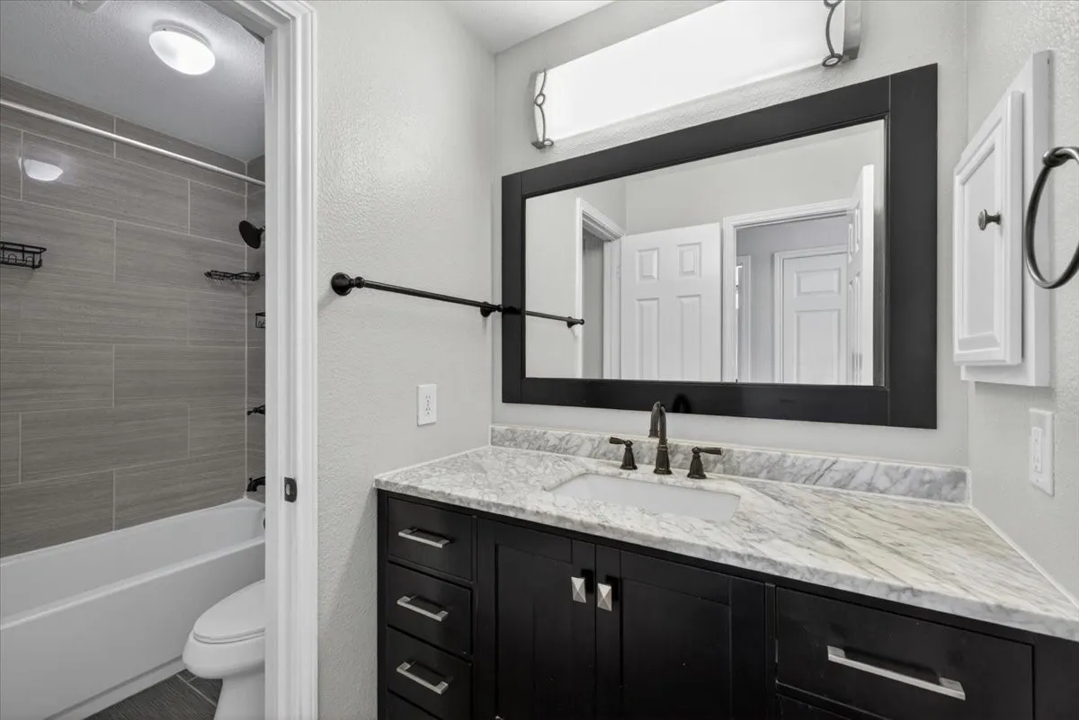 Bathroom featuring a dark wood-finish vanity with a light-toned countertop, a large framed mirror, and a tub-shower combination with grey subway tile surround