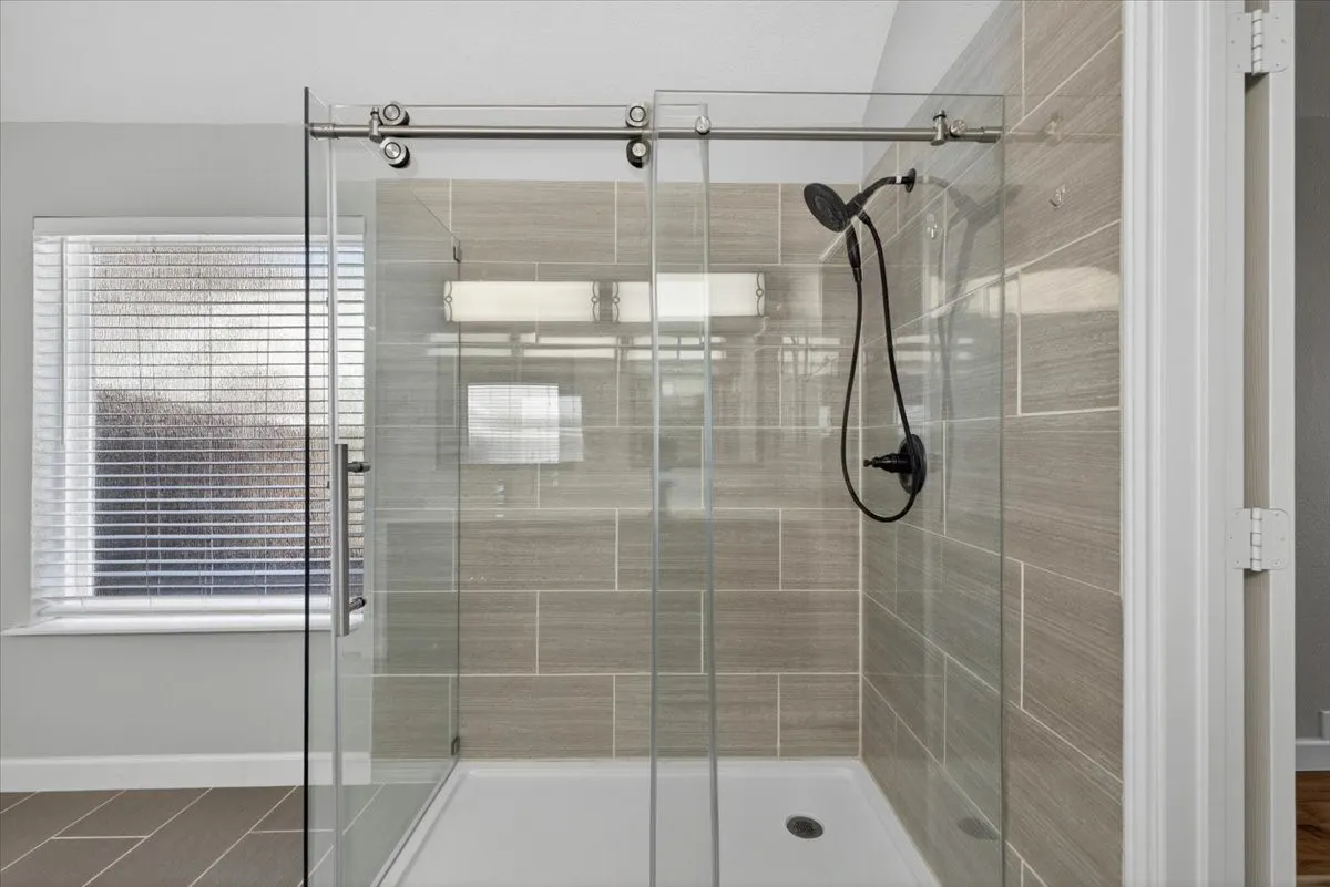 Glass-enclosed shower with sliding barn door hardware and a matte black shower fixture