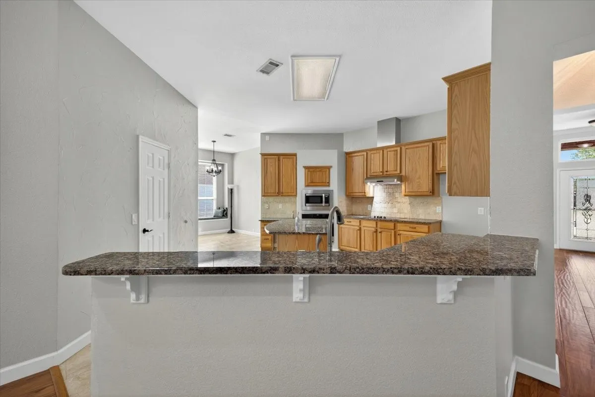 Kitchen featuring a granite-look breakfast bar, wood cabinetry, built-in microwave, and stainless steel appliances