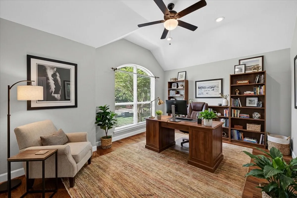 Office space featuring vaulted ceilings, a large arched window with exterior landscaping, recessed lighting, a ceiling fan, and wood-finish flooring