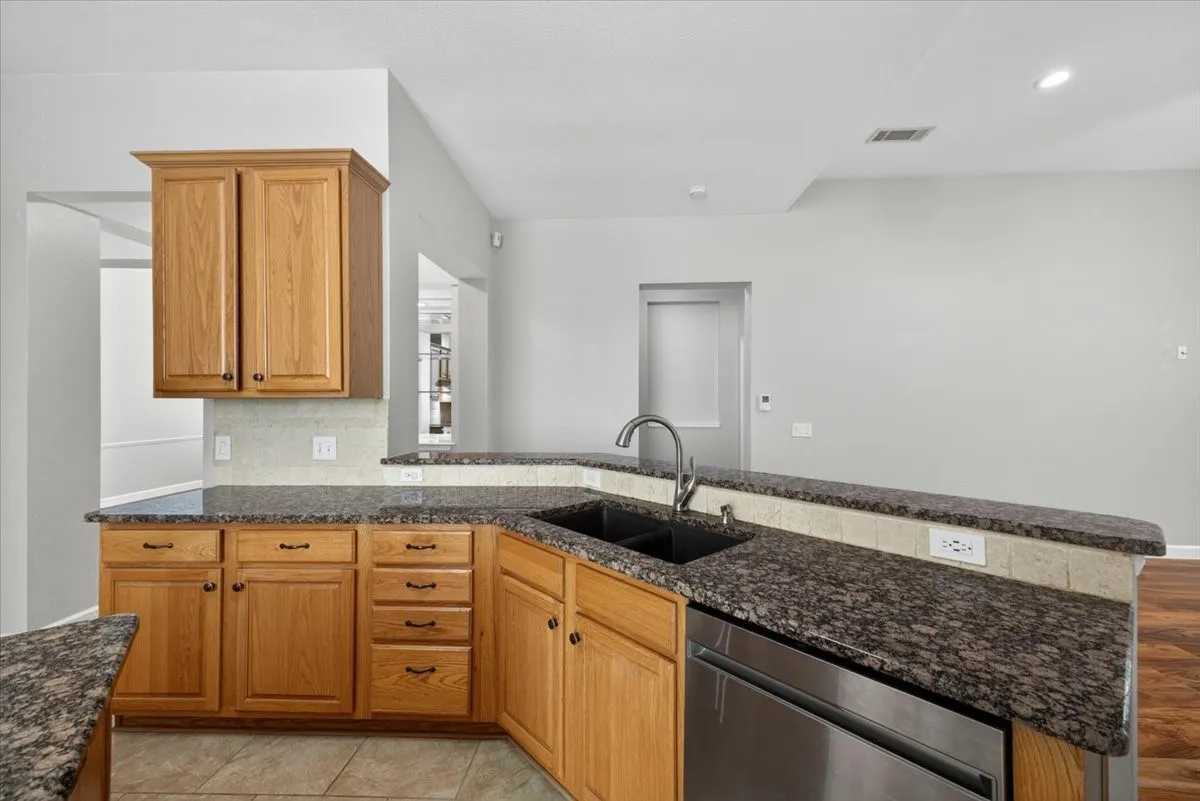 Kitchen featuring granite countertops, wood cabinetry, tile backsplash, stainless steel dishwasher, and a black sink with a gooseneck faucet