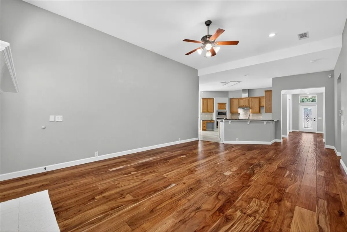 Spacious room featuring wood-finish flooring, vaulted ceilings, and a ceiling fan with integrated lighting