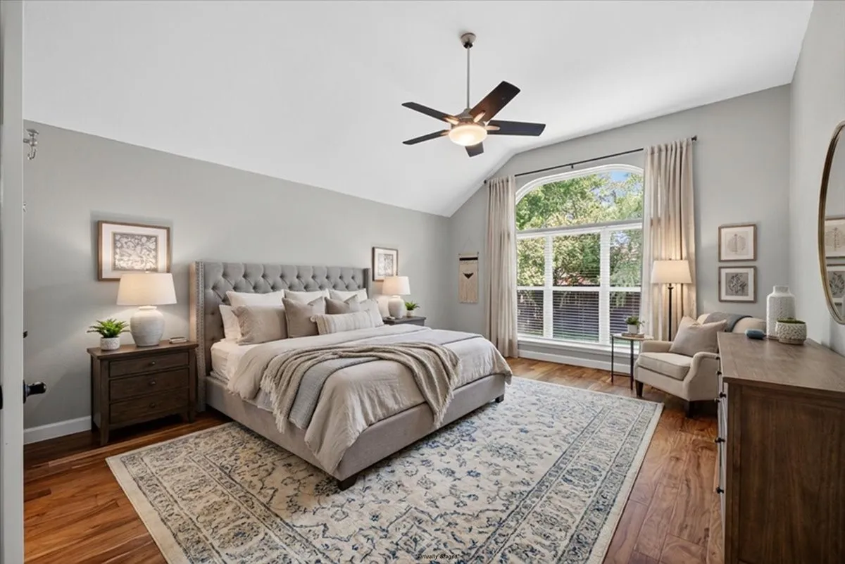 Vaulted ceiling room featuring hardwood flooring and a large arched window with exterior foliage