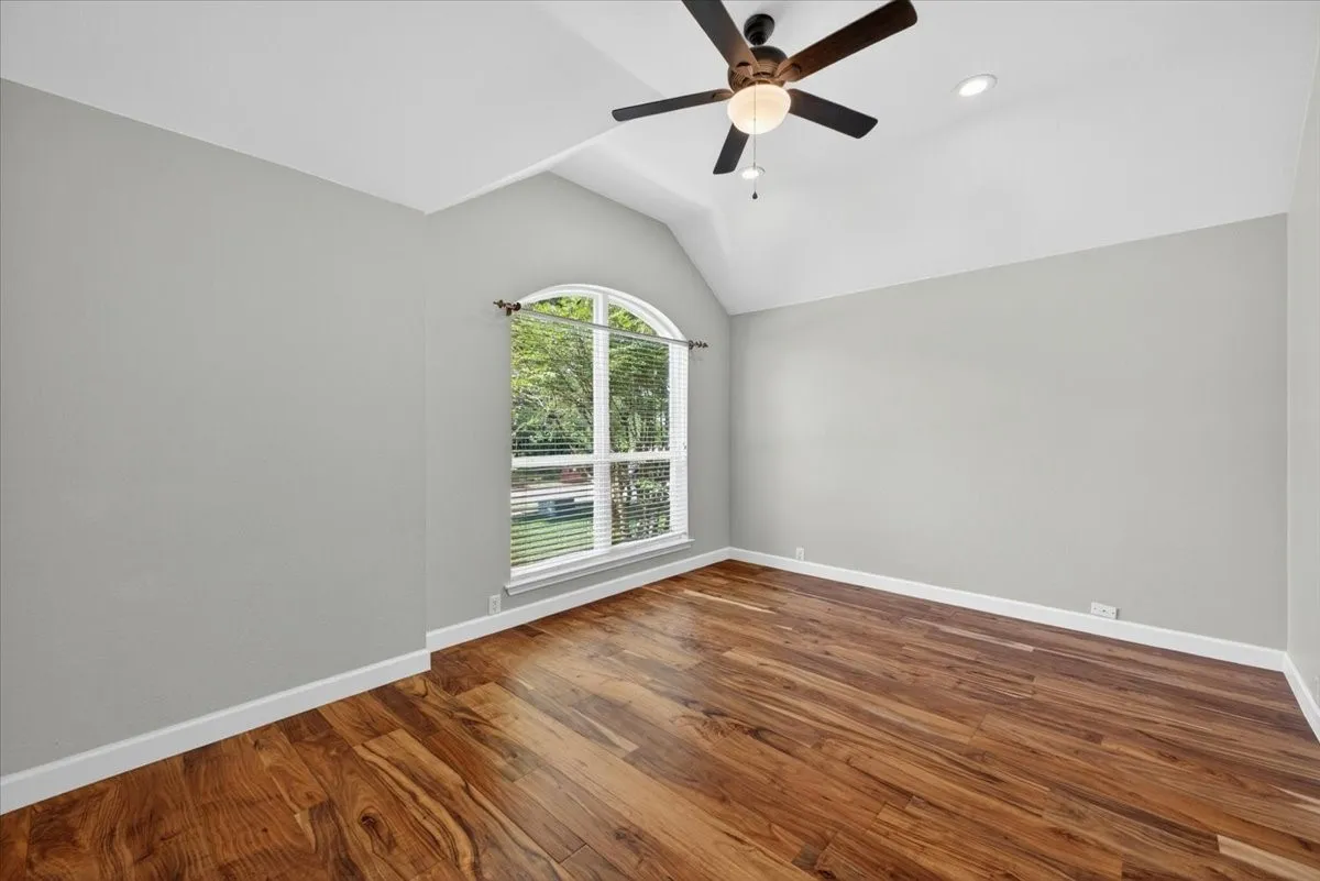 Room featuring a vaulted ceiling with a ceiling fan, a large arched window with blinds, wood-finish flooring, and recessed lighting