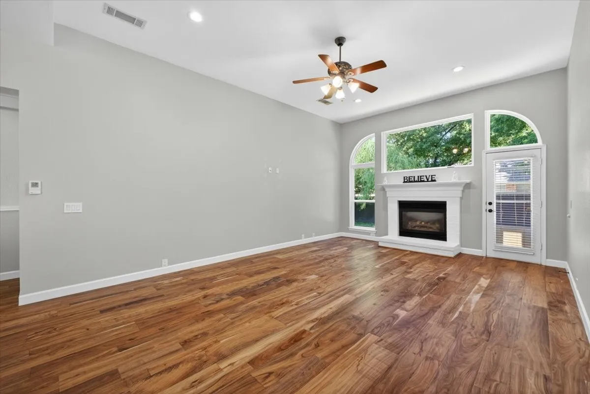 Spacious room featuring wood-finish flooring, a white mantel fireplace, and a ceiling fan