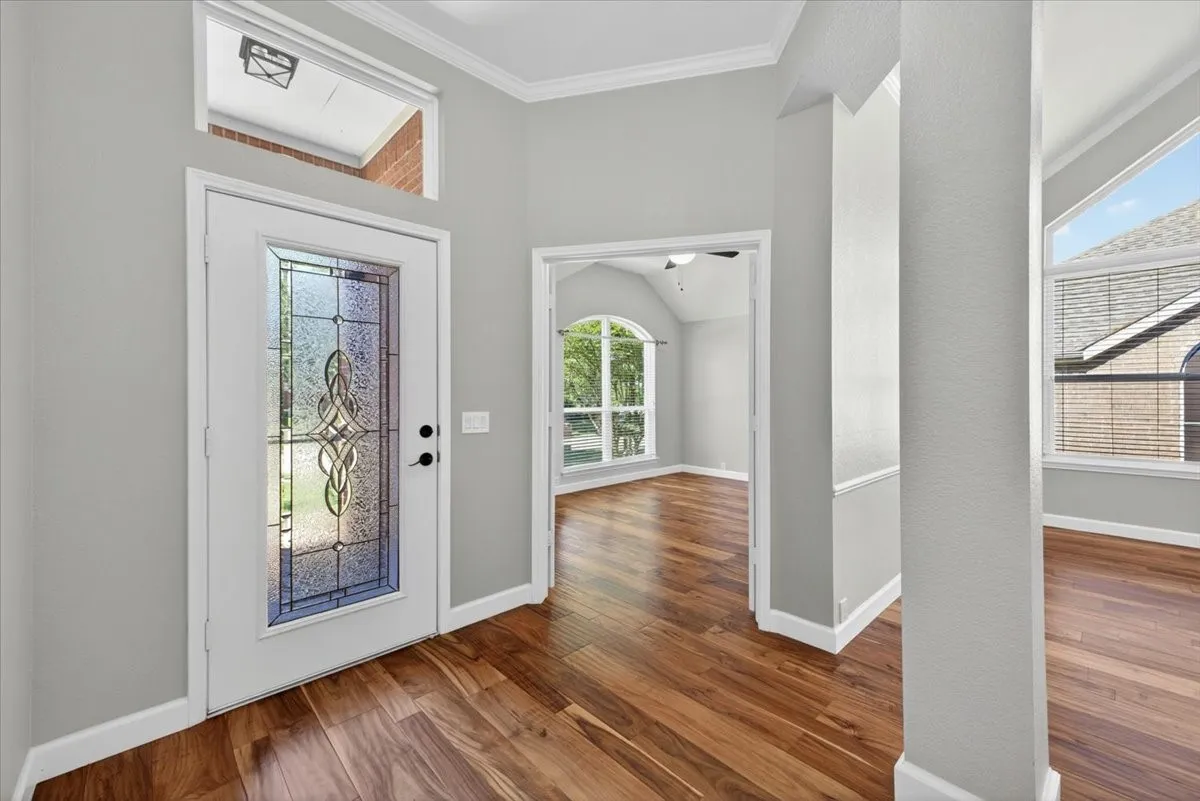 Entryway featuring a decorative glass panel door with transom window, wood-finish flooring, and crown molding