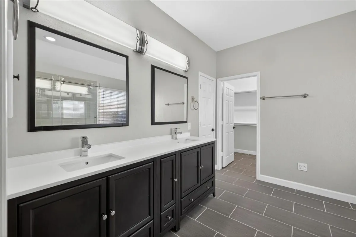 Bathroom featuring a double vanity with dark cabinetry, white countertops, and chrome fixtures