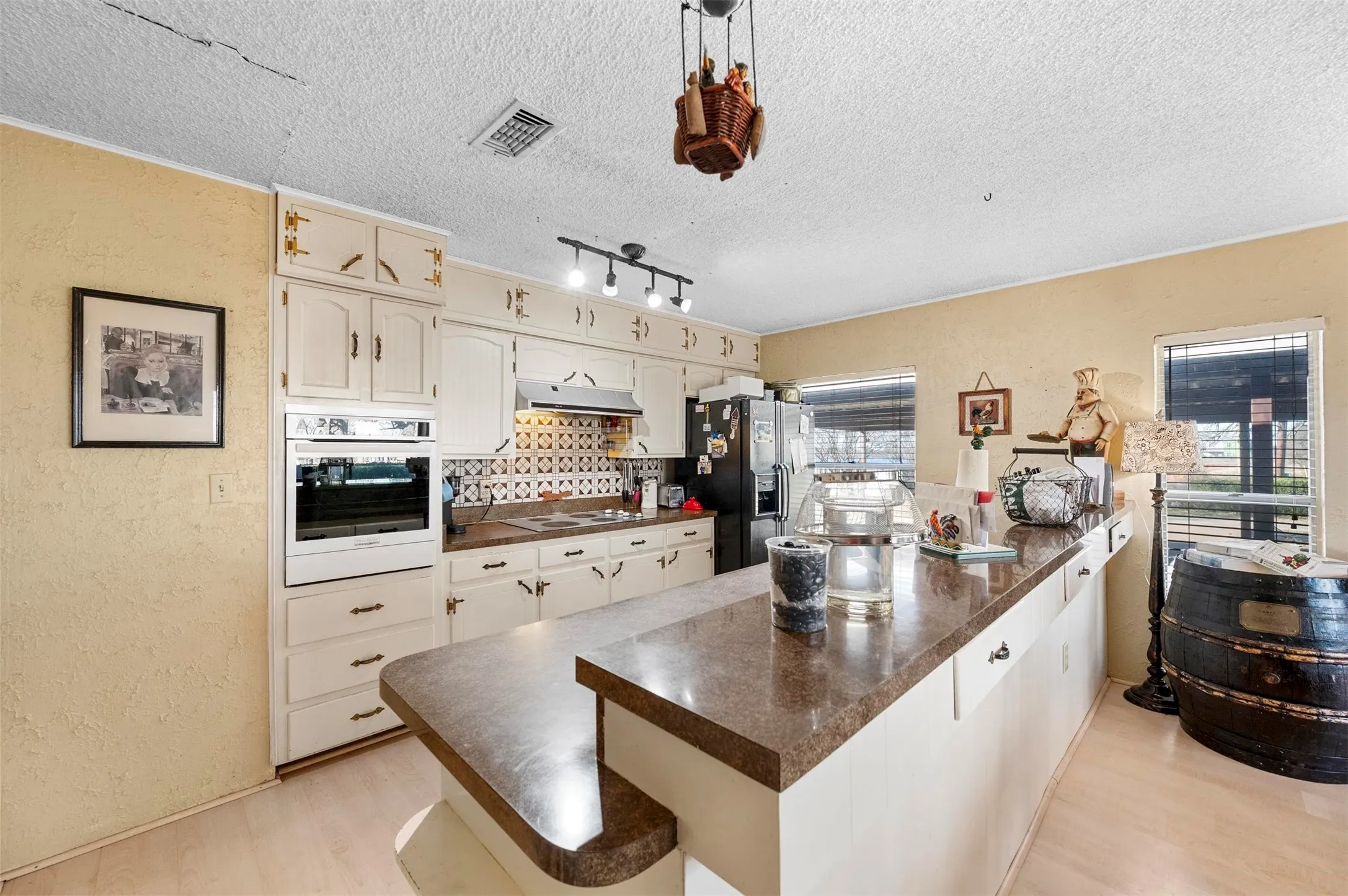 Kitchen featuring an extended island with a countertop, white cabinetry with decorative hardware, a tiled backsplash, and light wood-finish flooring