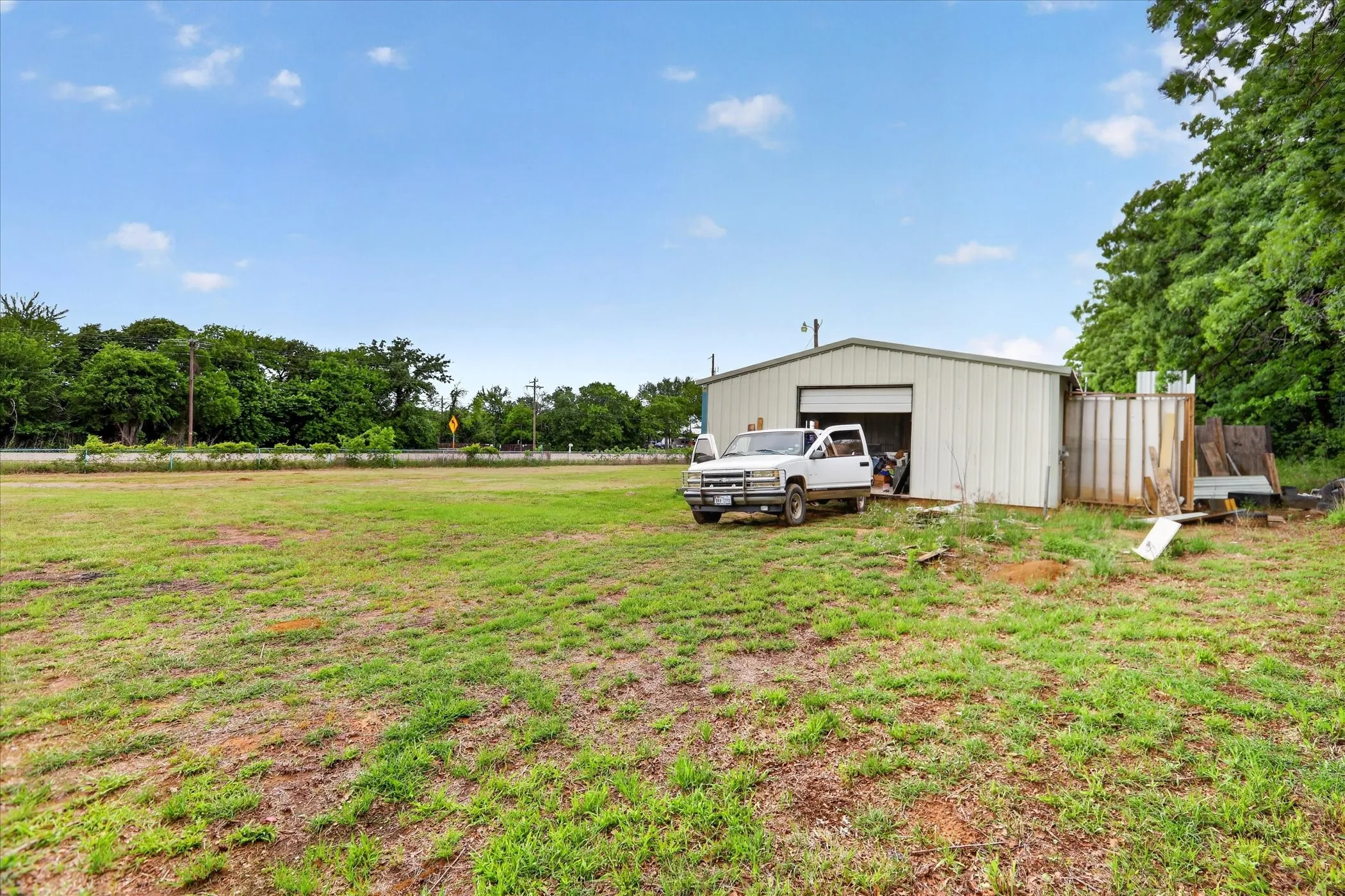 Expansive grassy lot featuring a metal outbuilding with a roll-up garage door and an adjacent covered storage area