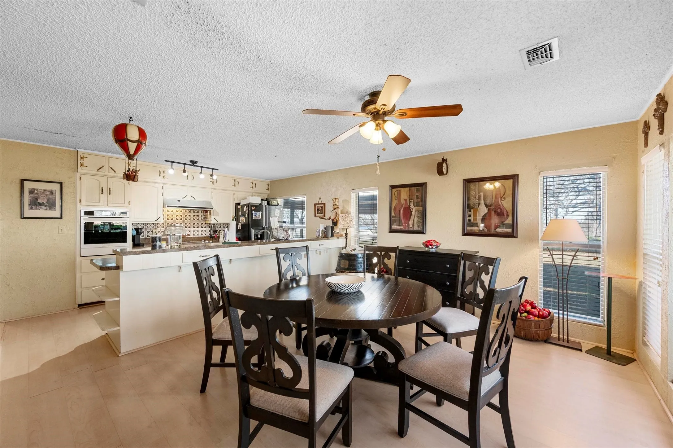 Kitchen and dining area featuring light-colored cabinetry, a built-in oven, and a tiled backsplash