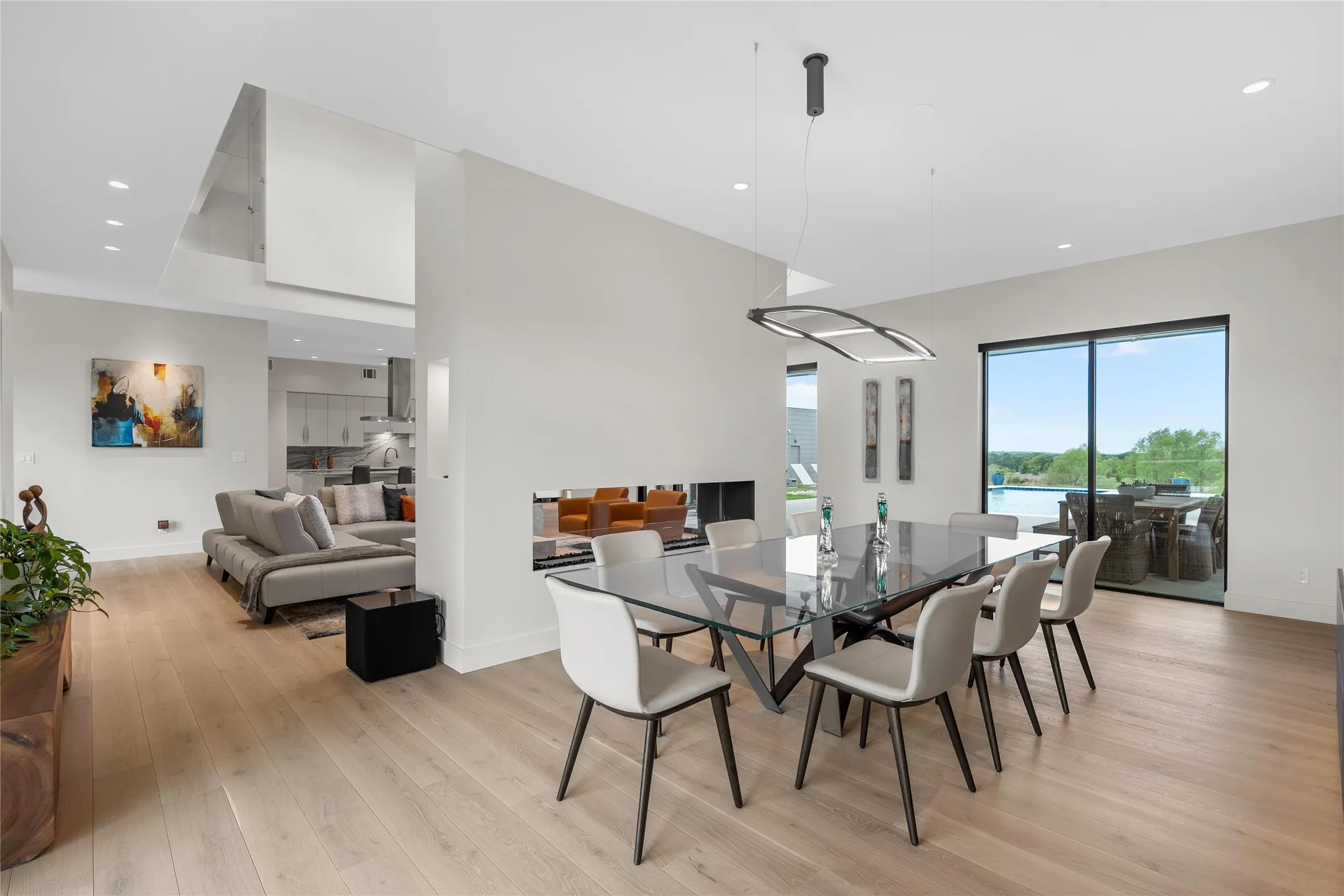 Open-concept dining area featuring wood-finish flooring, a contemporary linear chandelier, and expansive glass sliding doors