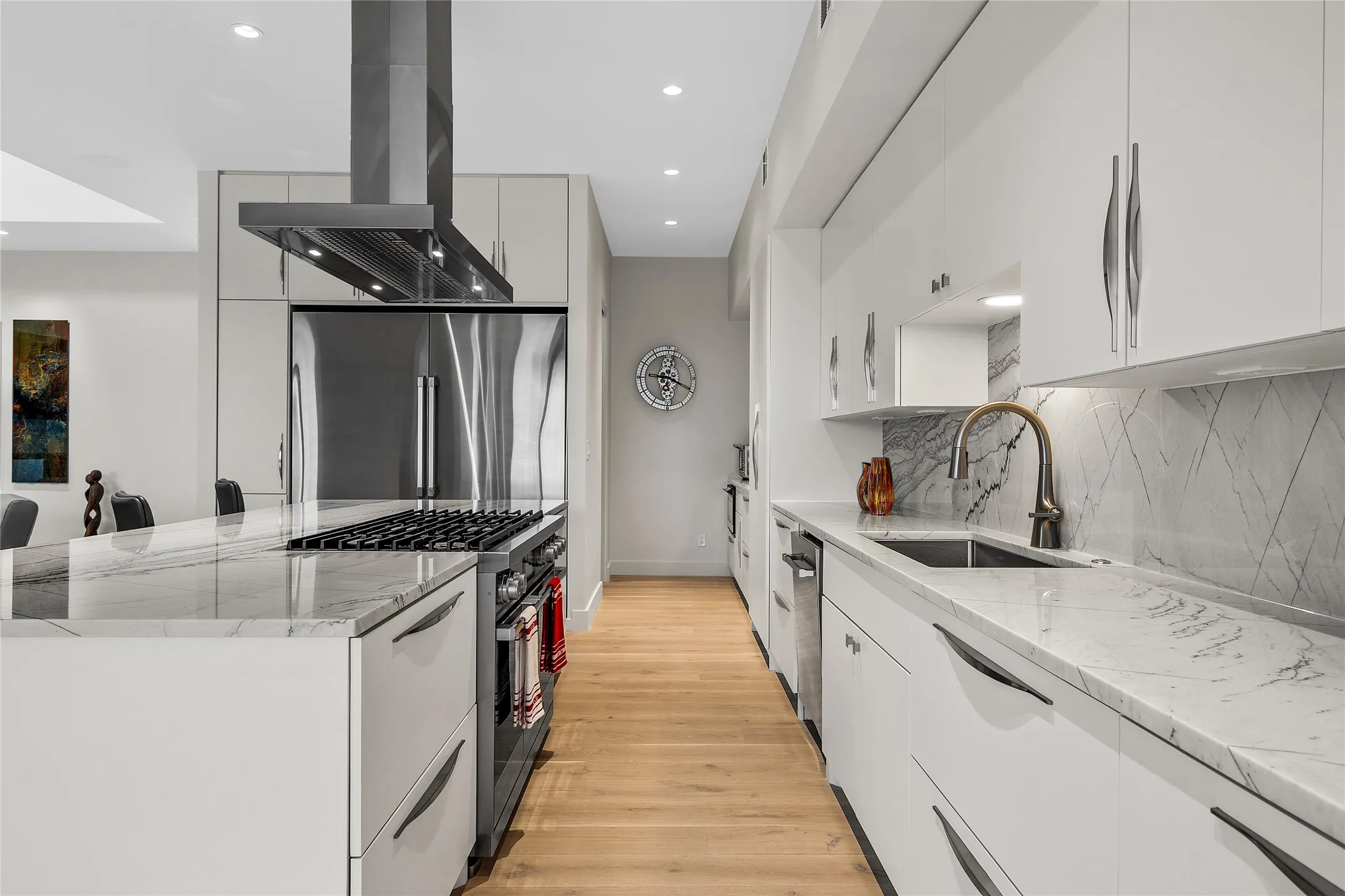 Modern kitchen featuring a stainless steel column refrigerator/freezer, 48” LP/electric range with overhead ventilation hood, and wood-finish flooring