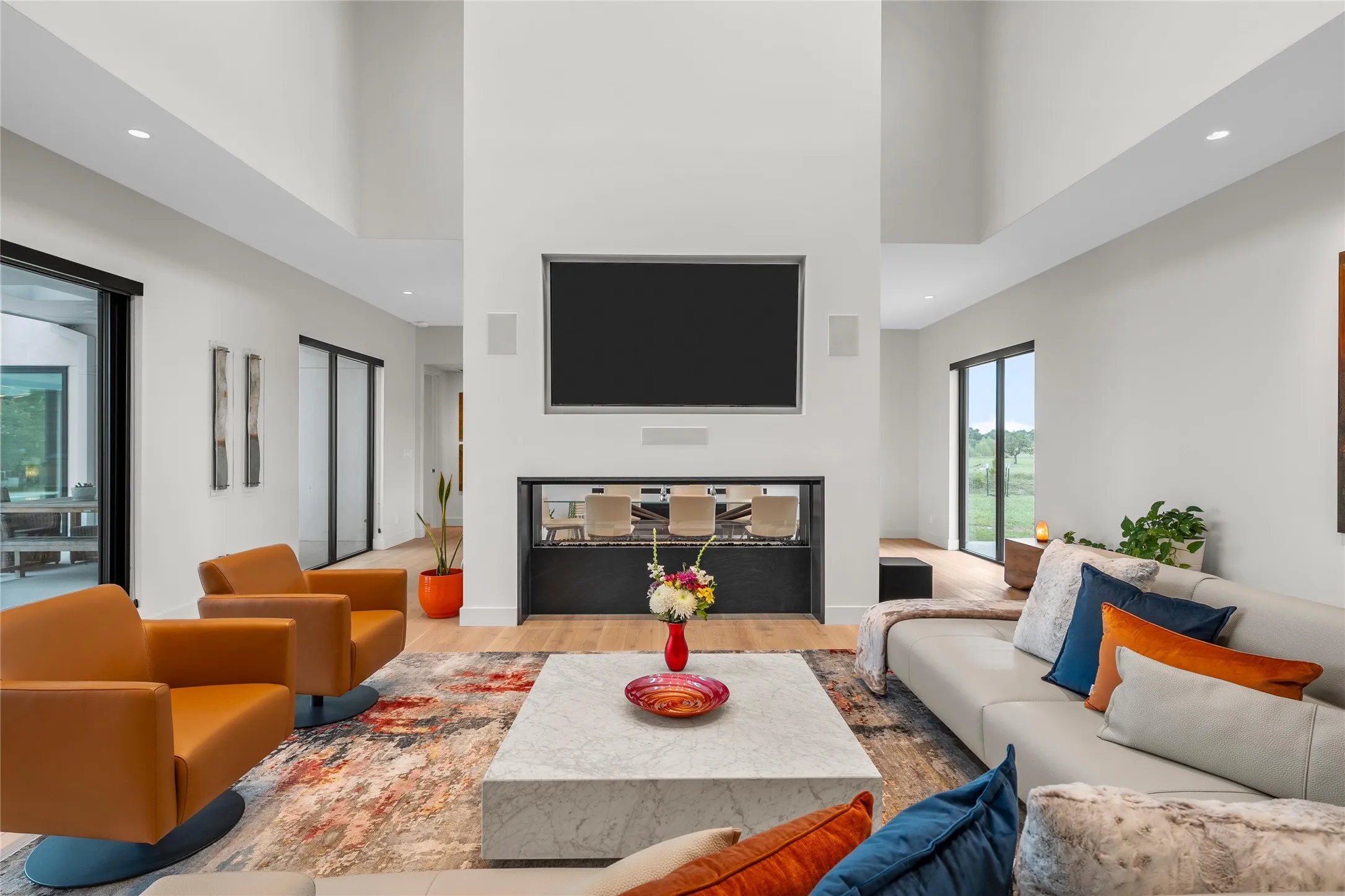 Spacious living area featuring a prominent fireplace with an integrated media center, high ceilings, large format sliding glass doors, recessed lighting, and wood-finish flooring