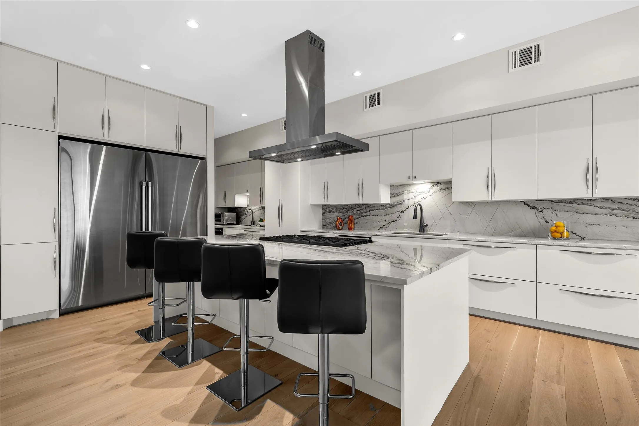 Contemporary kitchen featuring a large central island with seating, a 48” LP/electric range with a stainless steel range hood, stainless steel column refrigerator/freezer, lots of storage, and a Quartzite stone countertops/backsplash