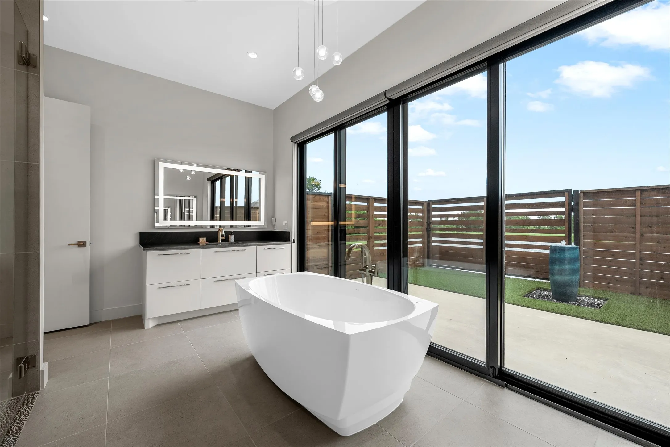 Modern bathroom featuring a freestanding soaking tub, a dual vanity with an illuminated mirror, and large format floor tiles