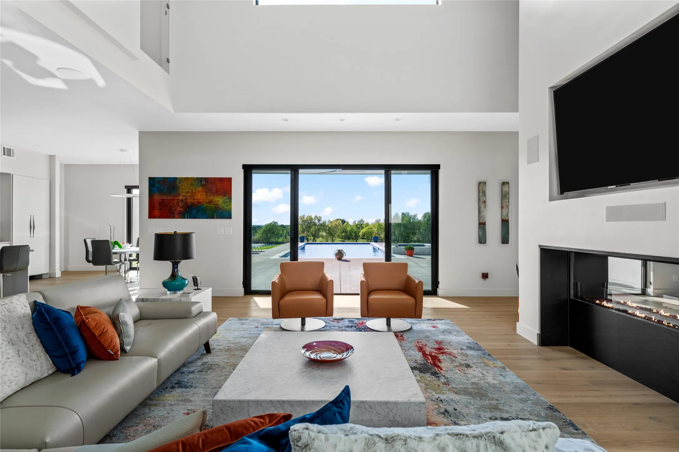 Spacious living area featuring high ceilings, wood-finish flooring, a linear fireplace, and expansive sliding glass doors opening to the exterior