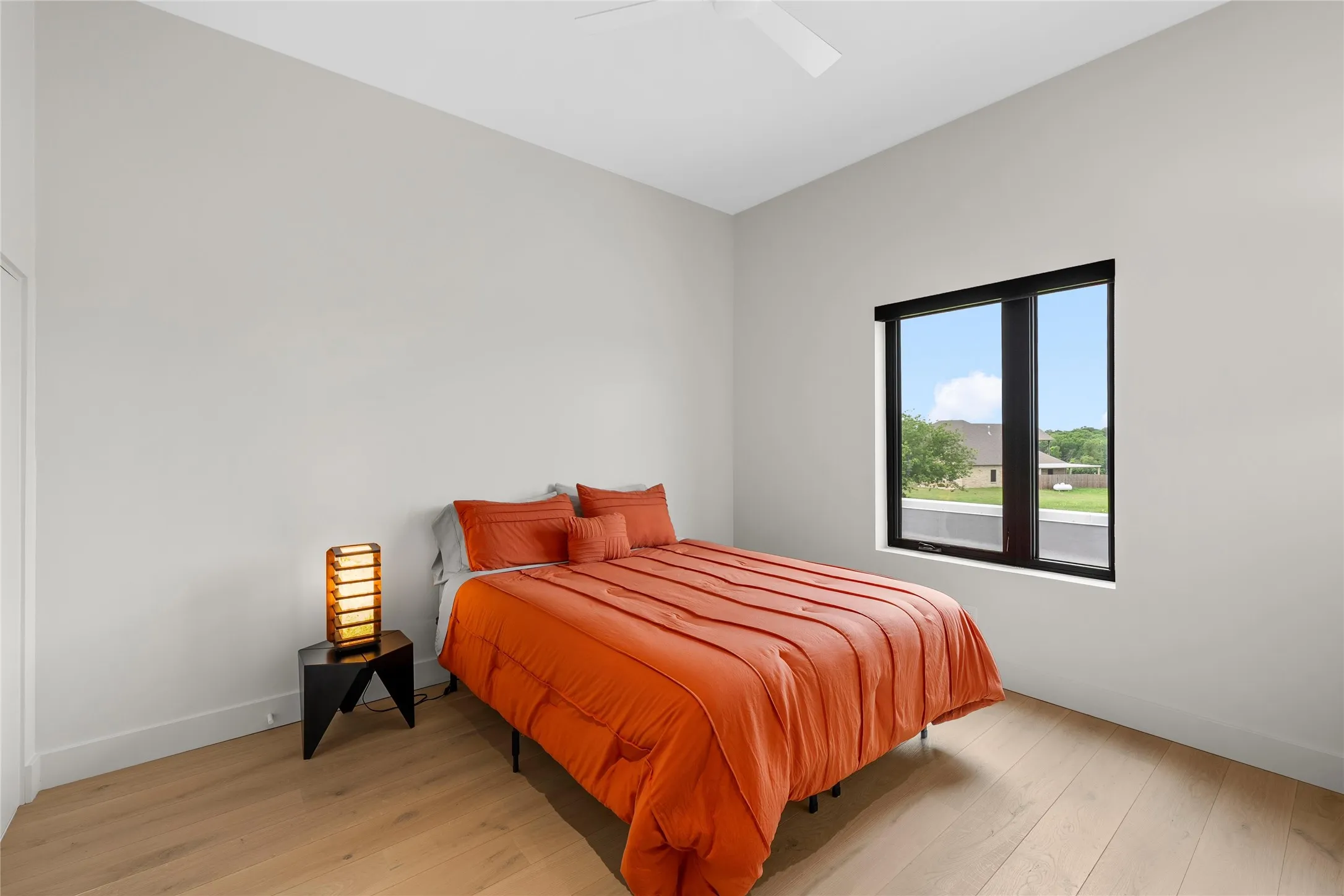 Bright bedroom featuring light wood-finish flooring, a contemporary black-framed window, and a white ceiling fan