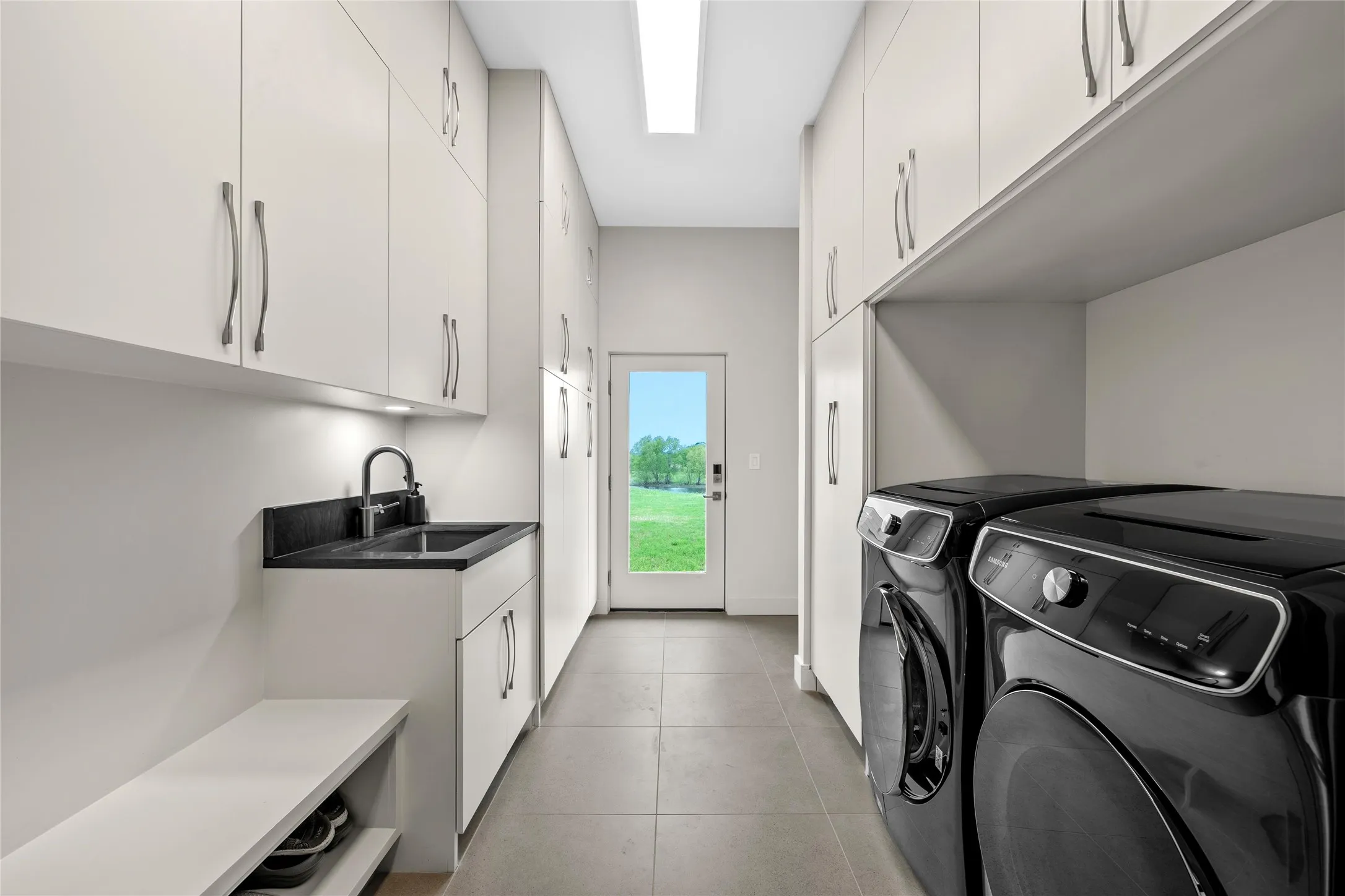 Utility room featuring extensive storage cabinetry, Quartzite countertop with an large sink and gooseneck faucet, light grey tile flooring, and a glass-paned door
