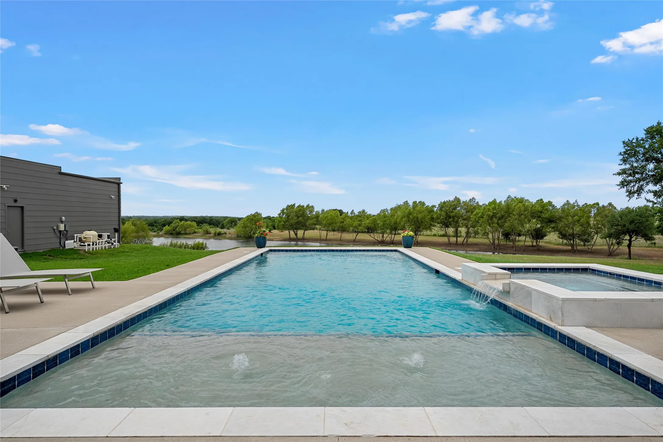 Outdoor swimming pool with an integrated spa, a water feature, and a shallow sun shelf, all bordered by a concrete patio