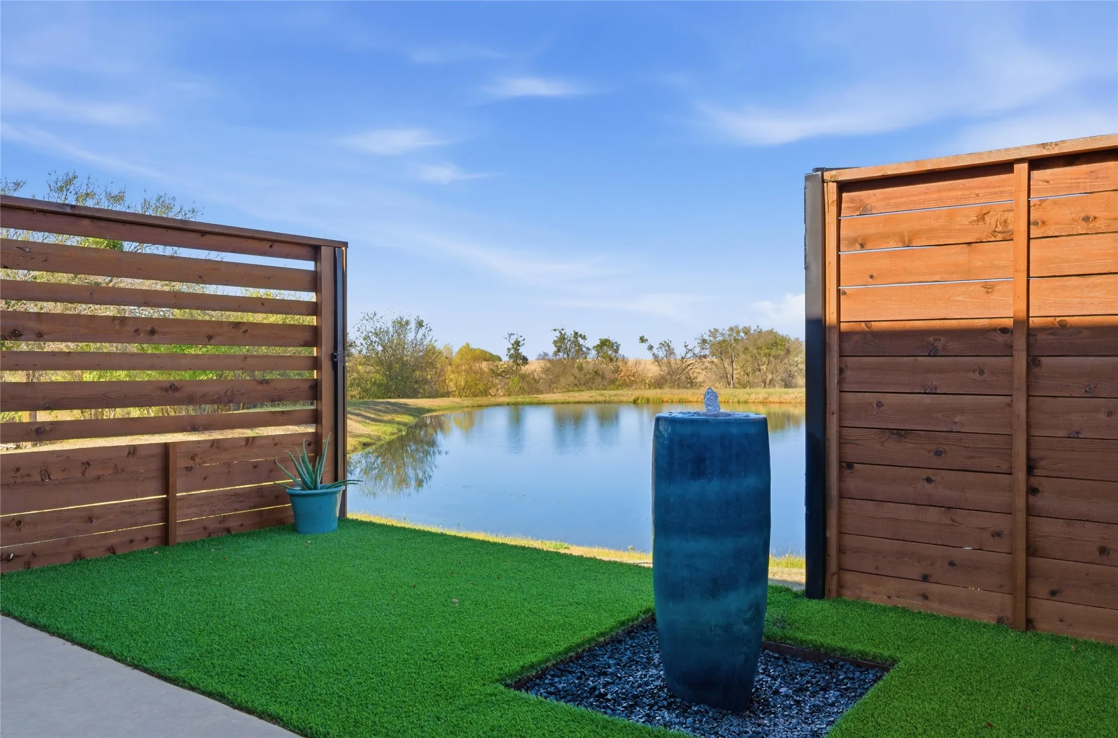 Outdoor space featuring a decorative water feature on a bed of dark stones, artificial turf, and wood privacy fencing