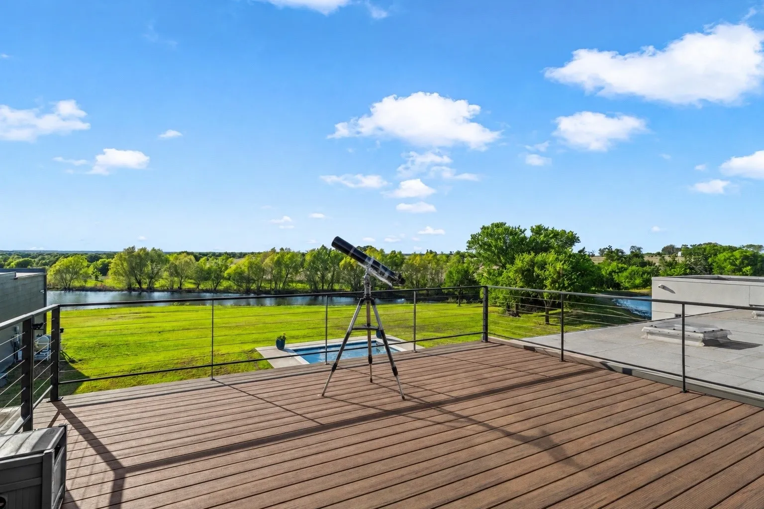 Expansive rooftop deck featuring composite wood-finish flooring, cable railings, and a concrete-surfaced area