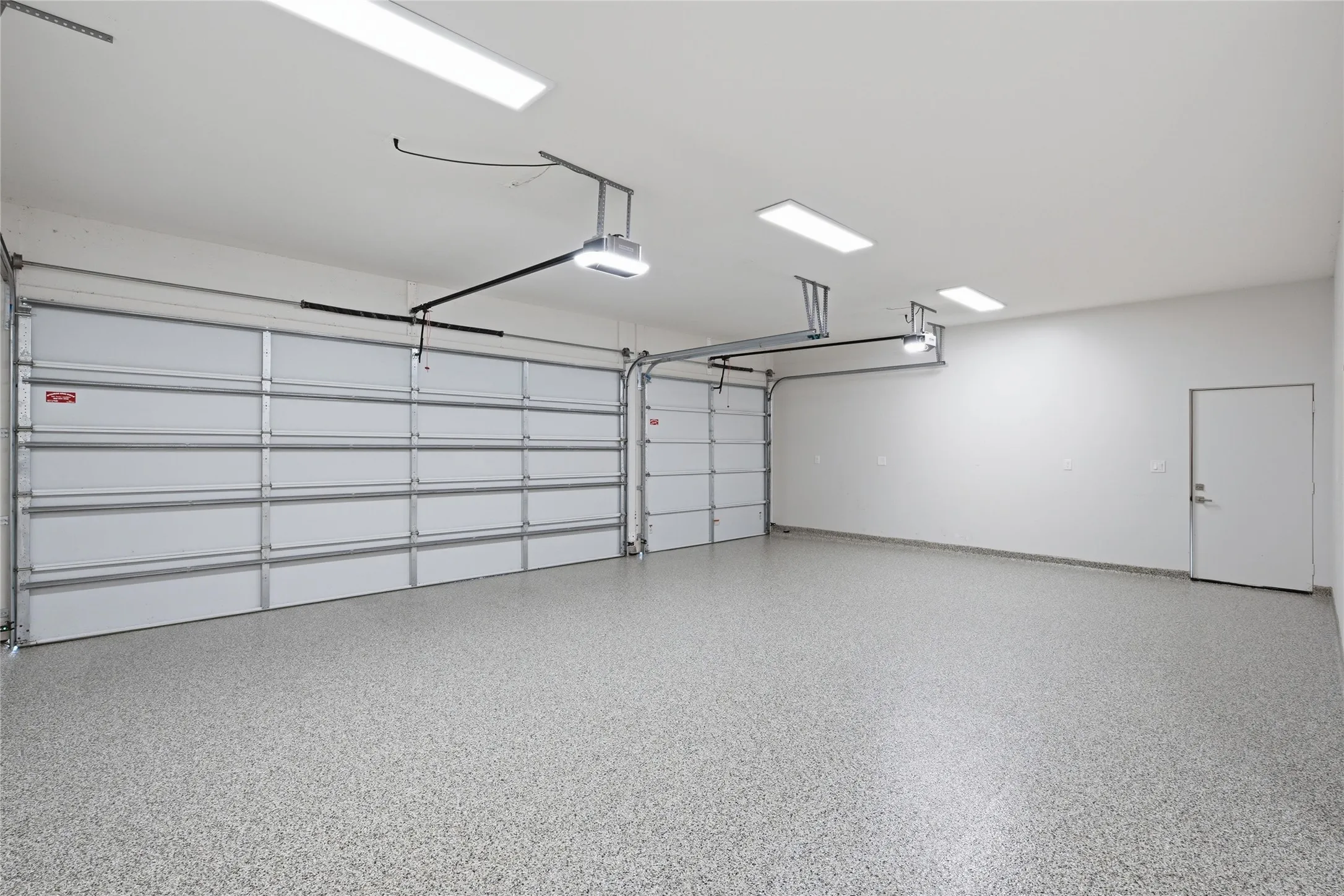 Spacious garage featuring two sectional overhead doors, a speckled epoxy floor coating, lots of lighting, under stairway climated-controlled storage closet, and a side access door to backyard
