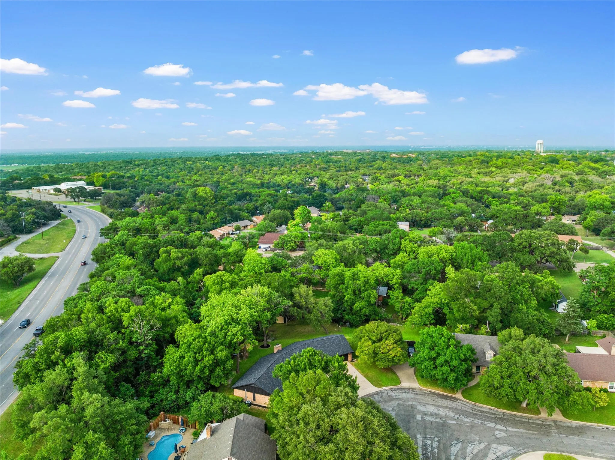 Aerial perspective showcasing a residential area enveloped by extensive tree coverage and a curved streetscape